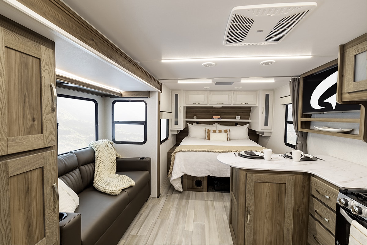Spacious, modern RV rental interior featuring a comfortable bed, living area with sofa, and compact kitchen/dining space.. Go Explore X203 2025