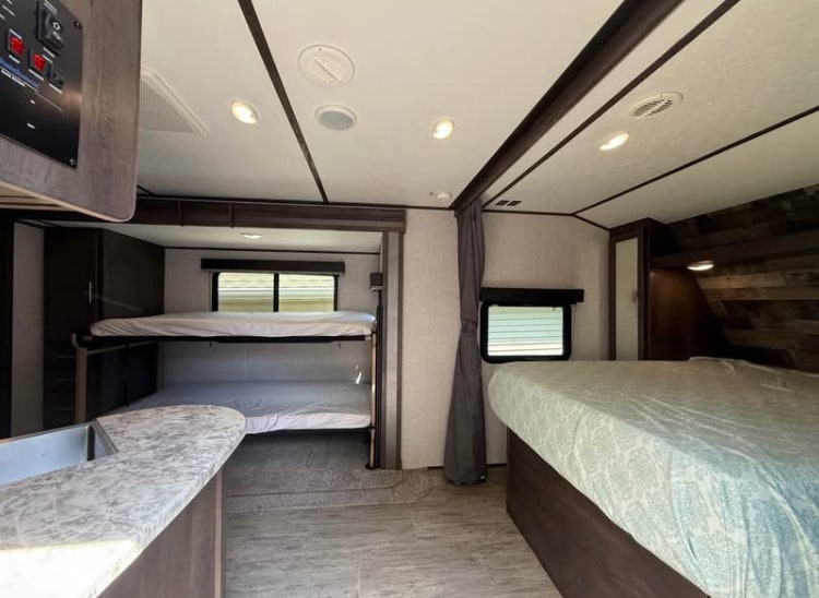 Discover this spacious RV rental interior, featuring bunk beds, a main bed, and a functional kitchen counter.. Dutchmen 2340BHS 2020