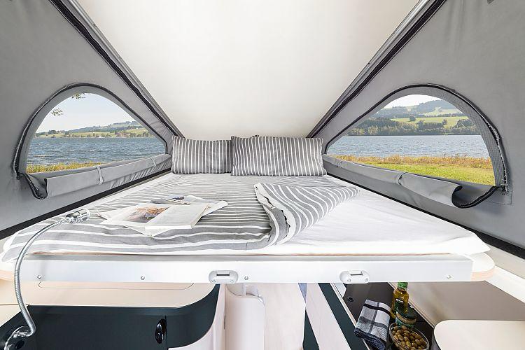 Enjoy the scenic outdoors in this RV rental! A pop-top camper offers a cozy bed with striped bedding and panoramic lake views.. Westfalia Westfalia Kepler One 2022