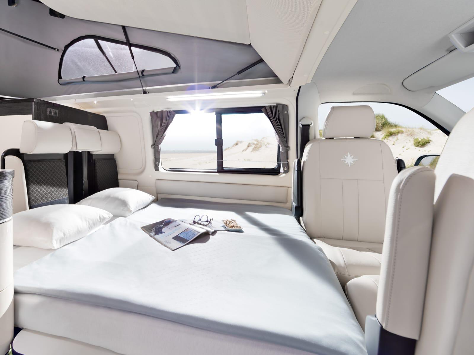 Inside a modern **rv rental**, featuring a comfortable bed, pop-top, and panoramic beach views from the windows.. Westfalia Westfalia Kepler One 2022