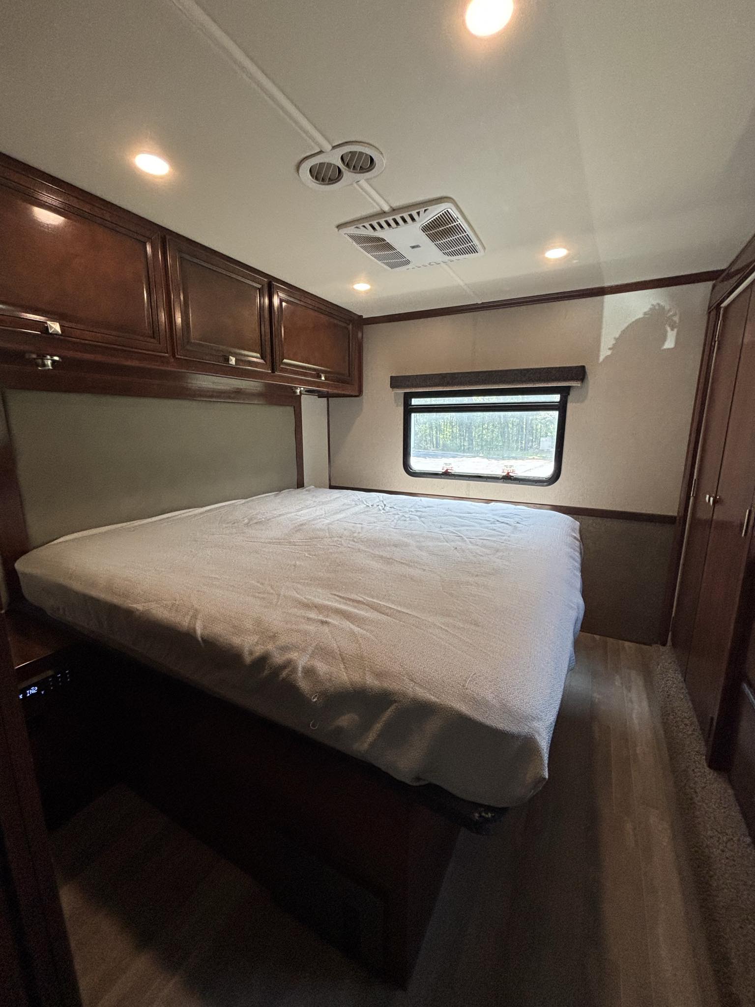 Step inside this RV rental's cozy bedroom, featuring a bed, ample overhead cabinets, a window with a tree view, & AC.. Holiday Rambler Admiral 2019