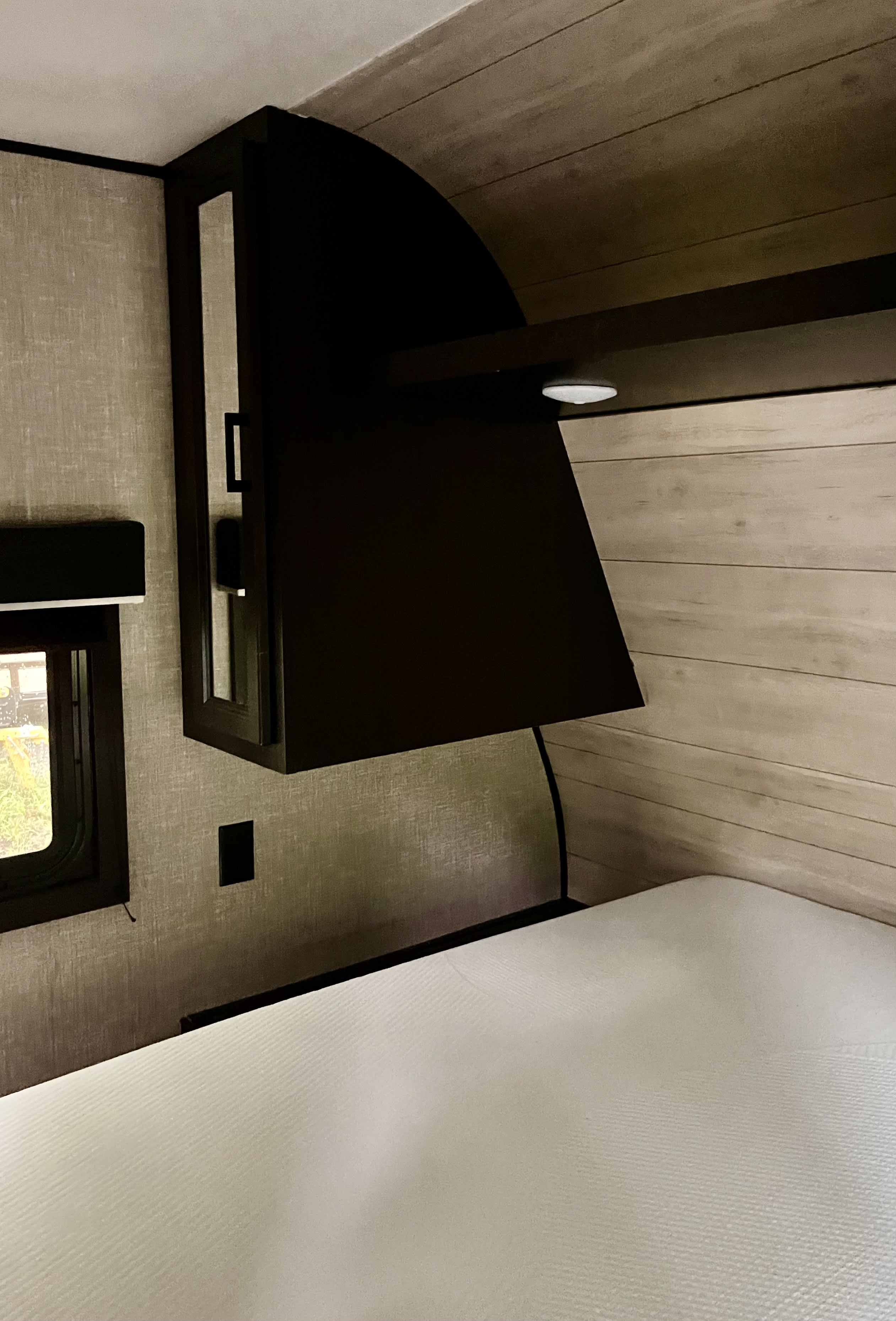 Interior of an RV rental bedroom: features a clean bed, dark overhead storage with lighting, and light textured walls.. Jayco Jay Flight SLX 2022