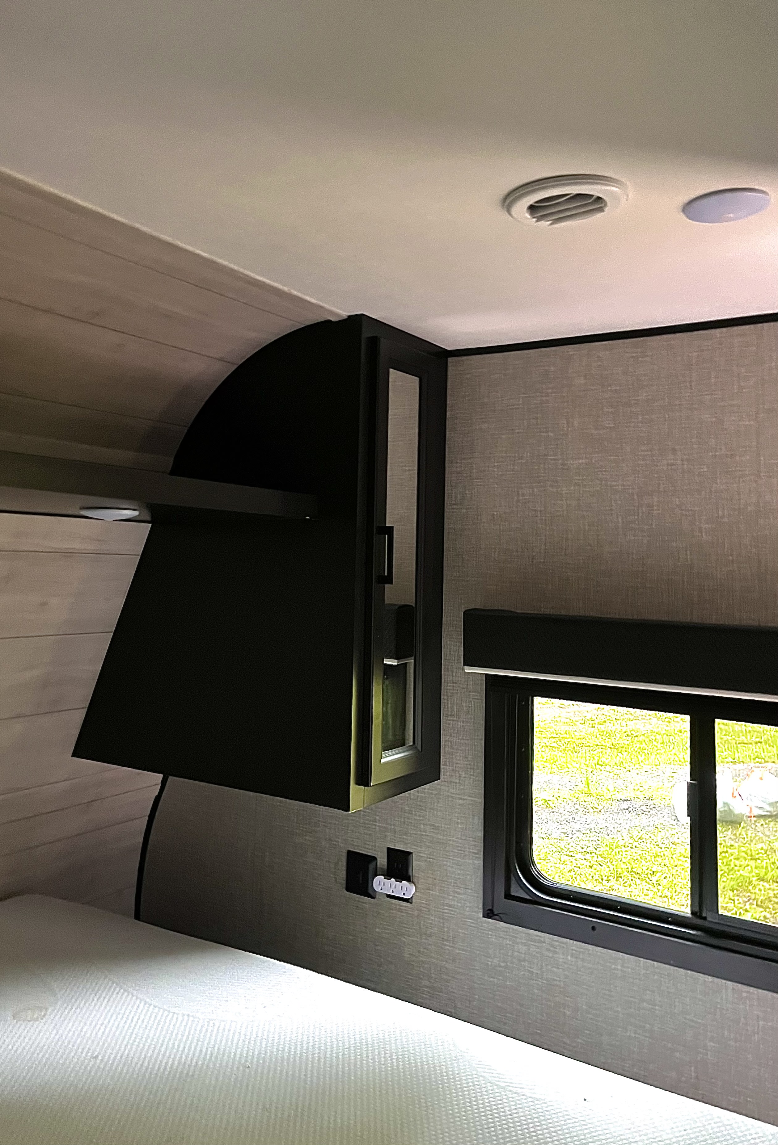 RV rental bedroom: light-wood and gray walls, bed, dark overhead storage with a window view. Ceiling AC vent.. Jayco Jay Flight SLX 2022