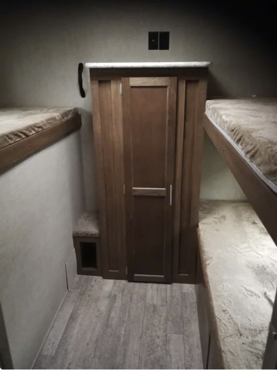 RV rental interior: A wooden wardrobe stands central, flanked by bunk beds, with a small carpeted step and wood-look flooring.. Grand River 32BHS 2019