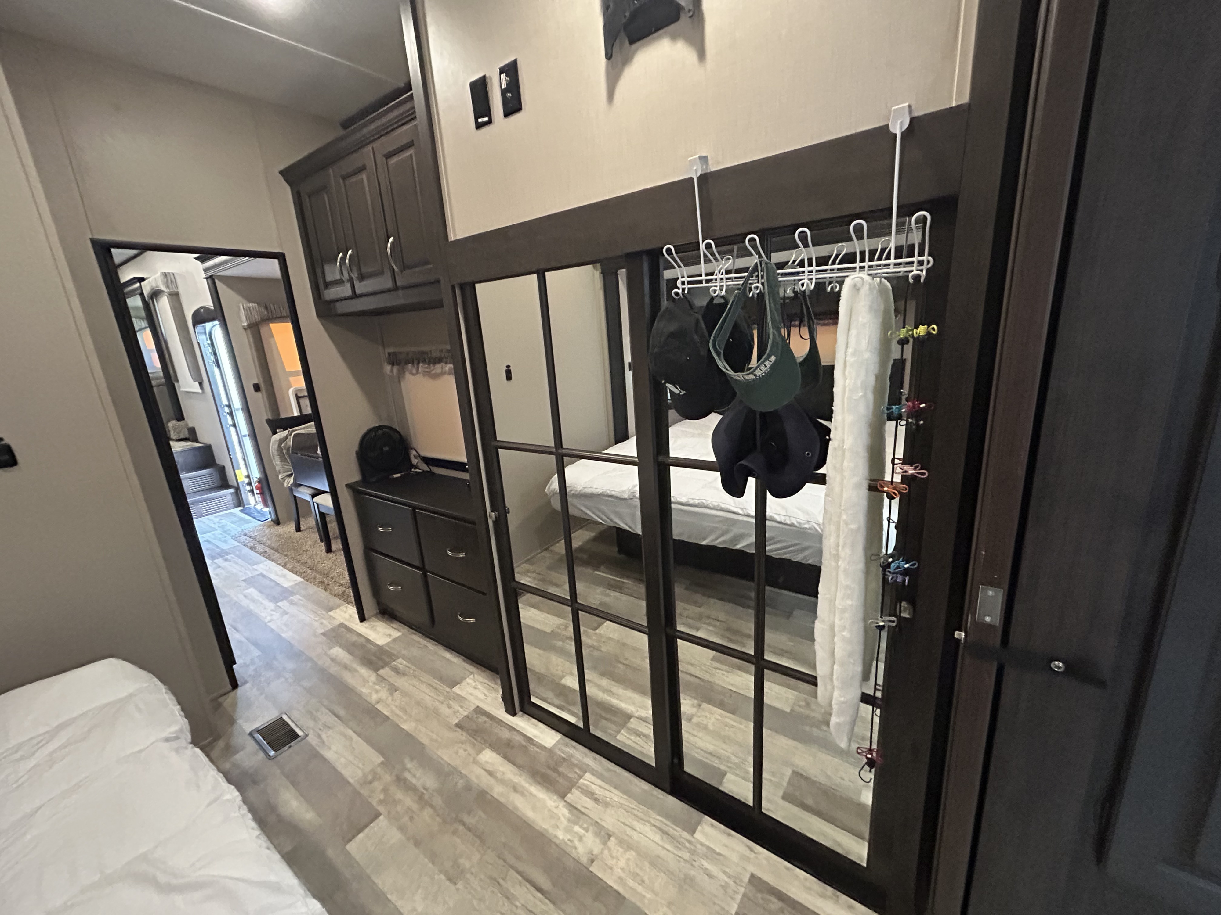 Inside an RV rental: a cozy bedroom with mirrored closet doors displaying hats, next to a dresser & living area.. Forest River Coachmen Brookstone 2021