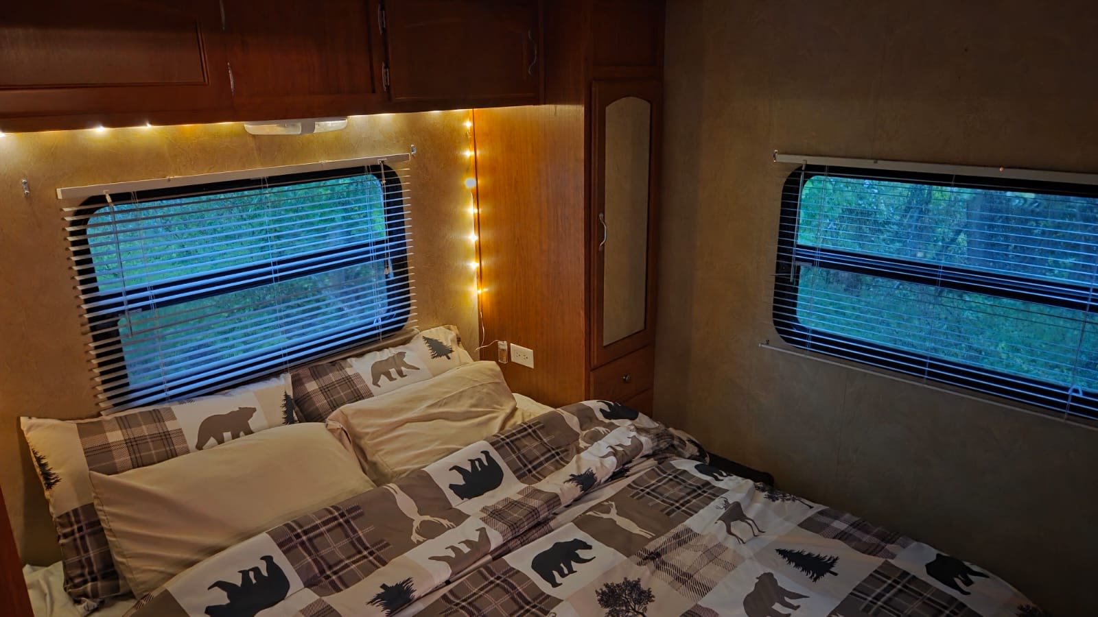 Cozy RV rental bedroom features bear & plaid bedding, string lights, and windows viewing nature. Perfect for an adventure.. Forest River Wildwood LA 2009