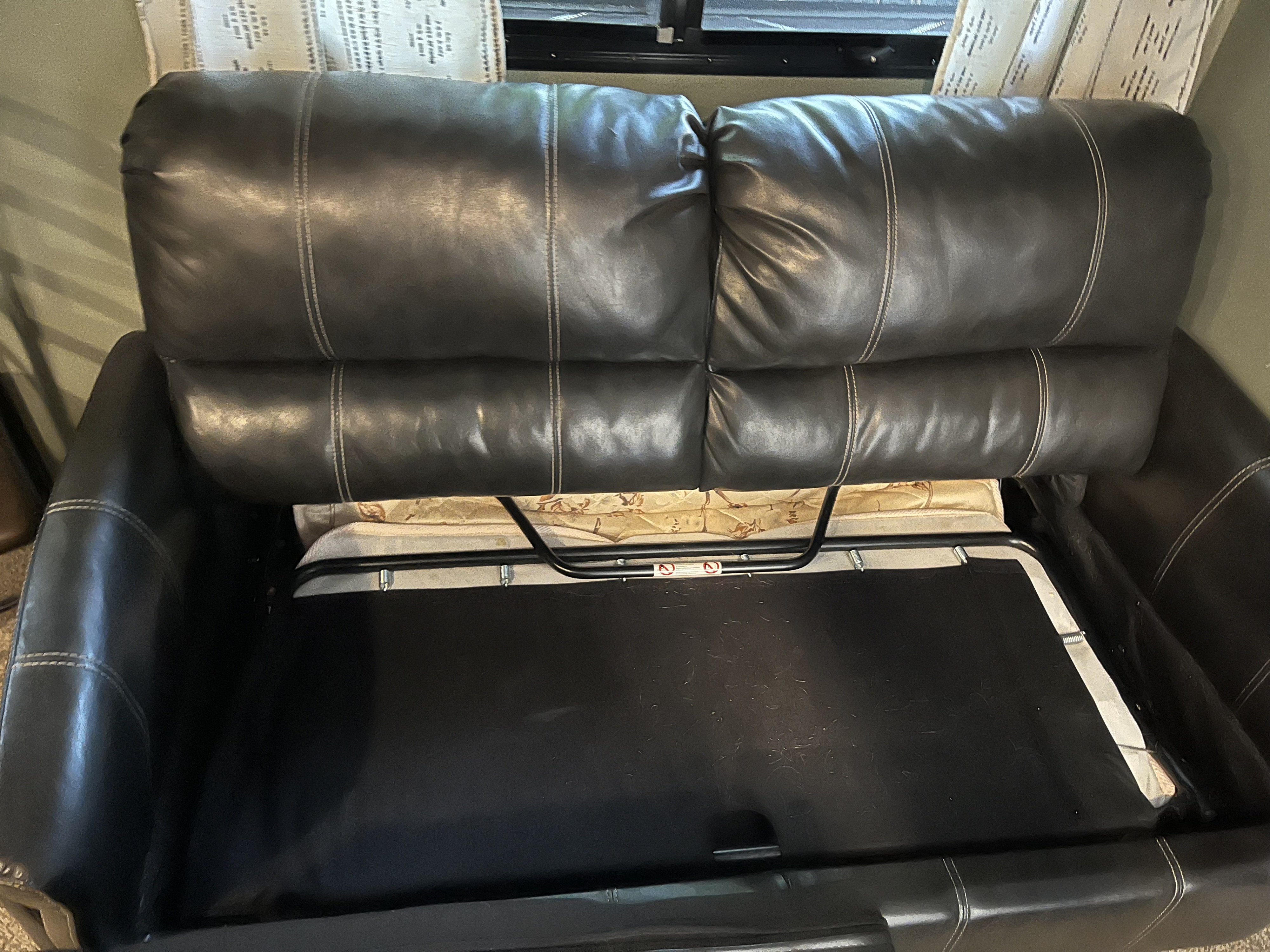 This RV rental features a dark leather pull-out sofa bed, partially open to reveal the mattress.. Forest River Tracer Breeze 2019