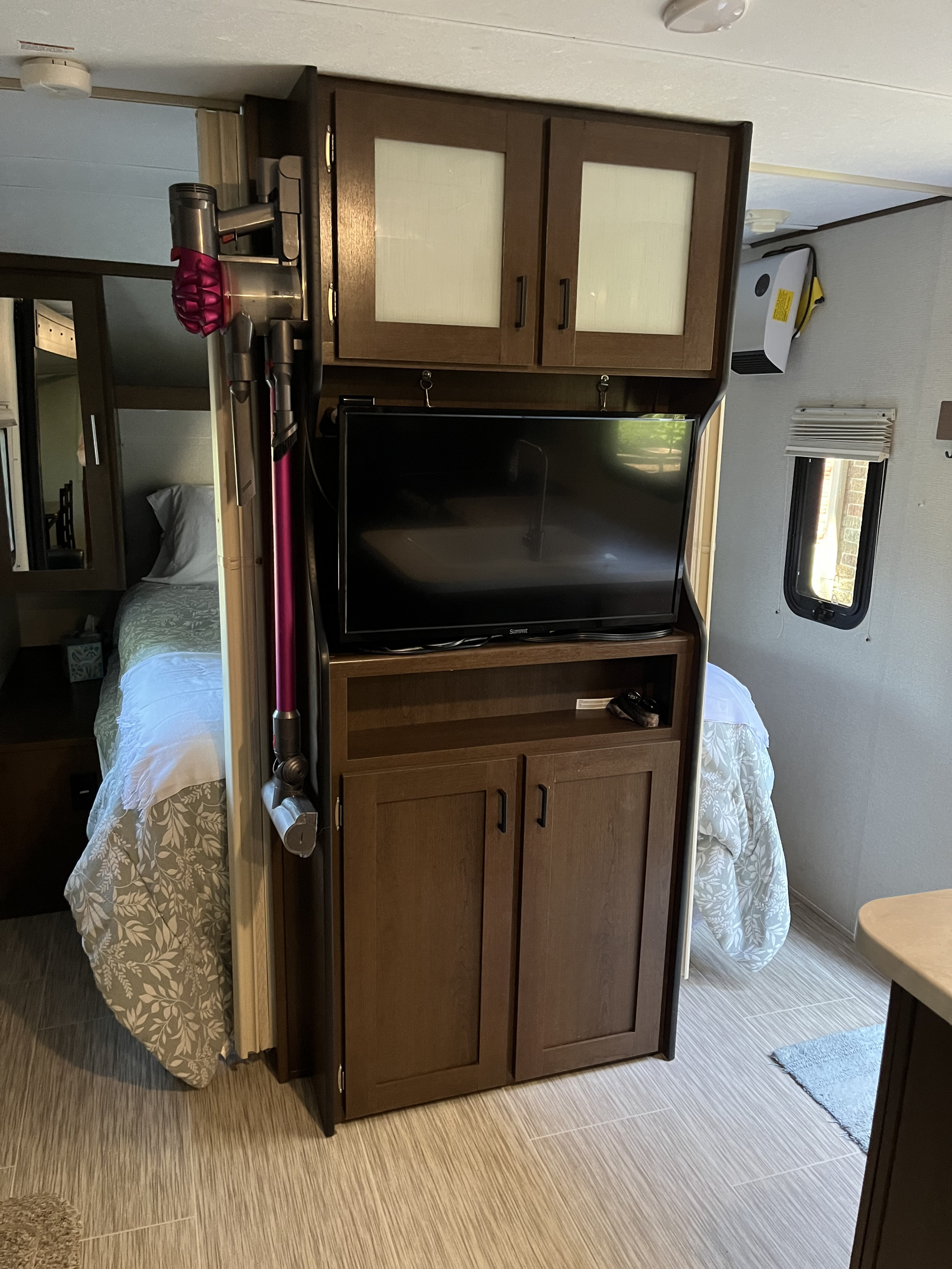 RV rental interior showing a compact living space with a TV, storage, Dyson vacuum, and adjacent sleeping areas.. Forest River Tracer Breeze 2019