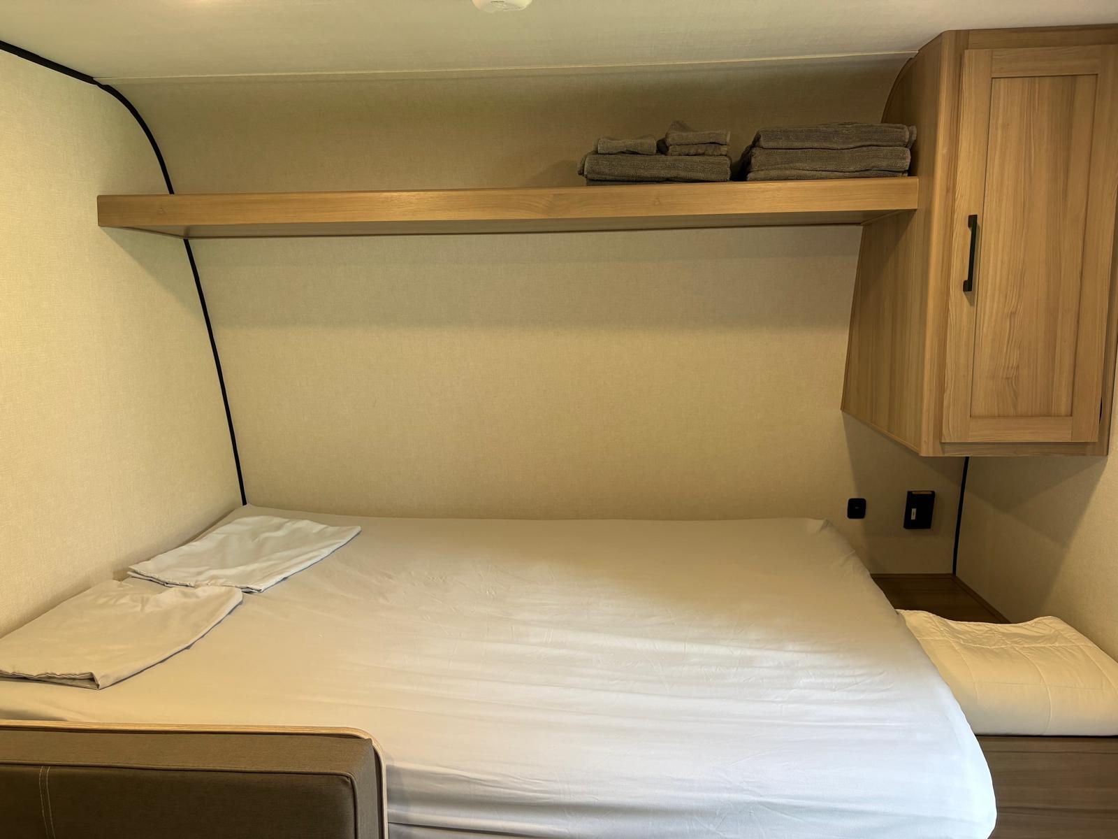 Cozy RV rental bedroom with a comfy bed, overhead shelf, and storage cabinet. Perfect for travel accommodation.. Keystone RV COLEMAN 17BX 2024