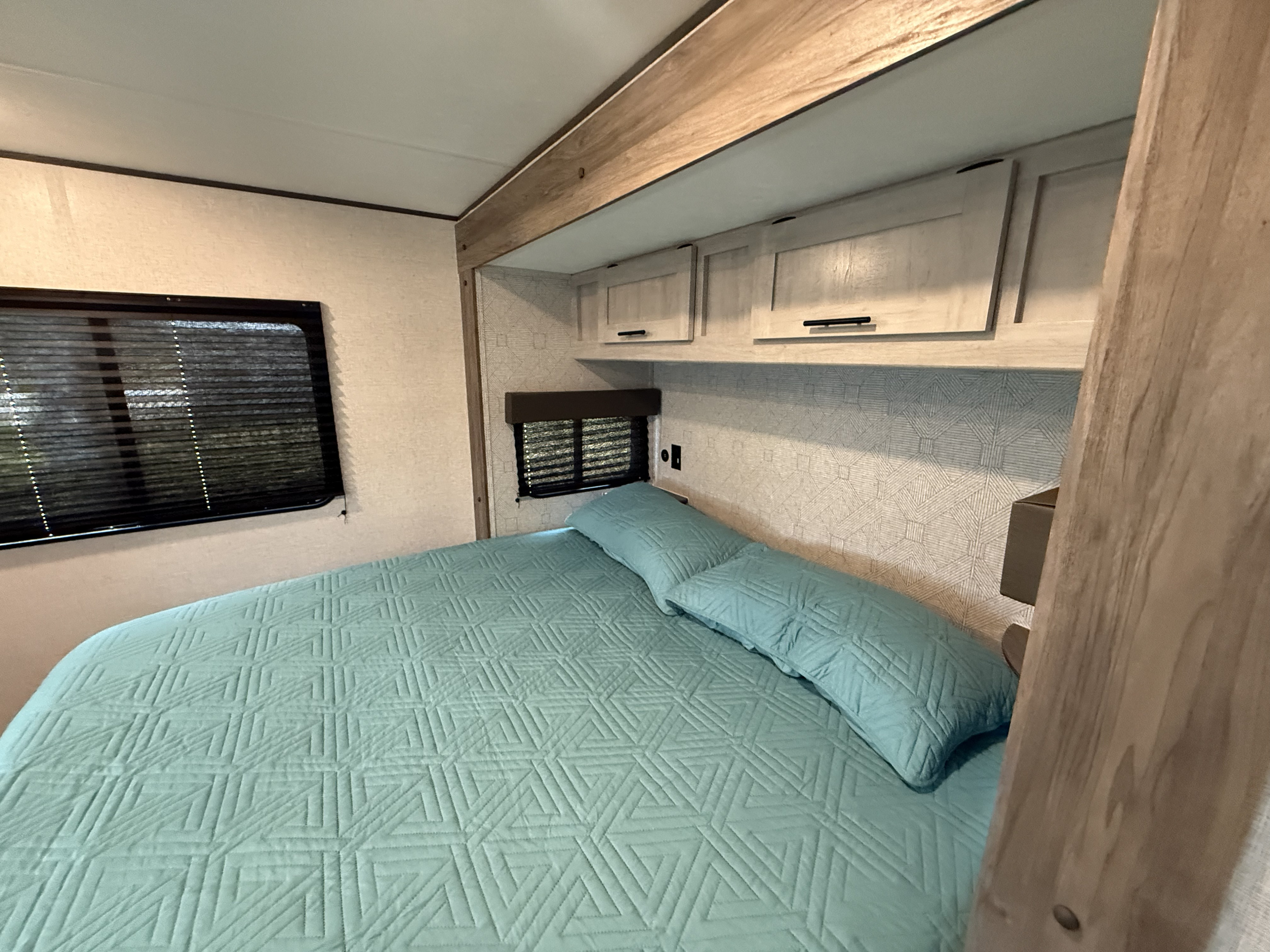 Comfortable RV rental bedroom featuring light blue bedding, dual windows, and ample storage, ideal for travel accommodations.. Heartland Zinger 320FB 2025