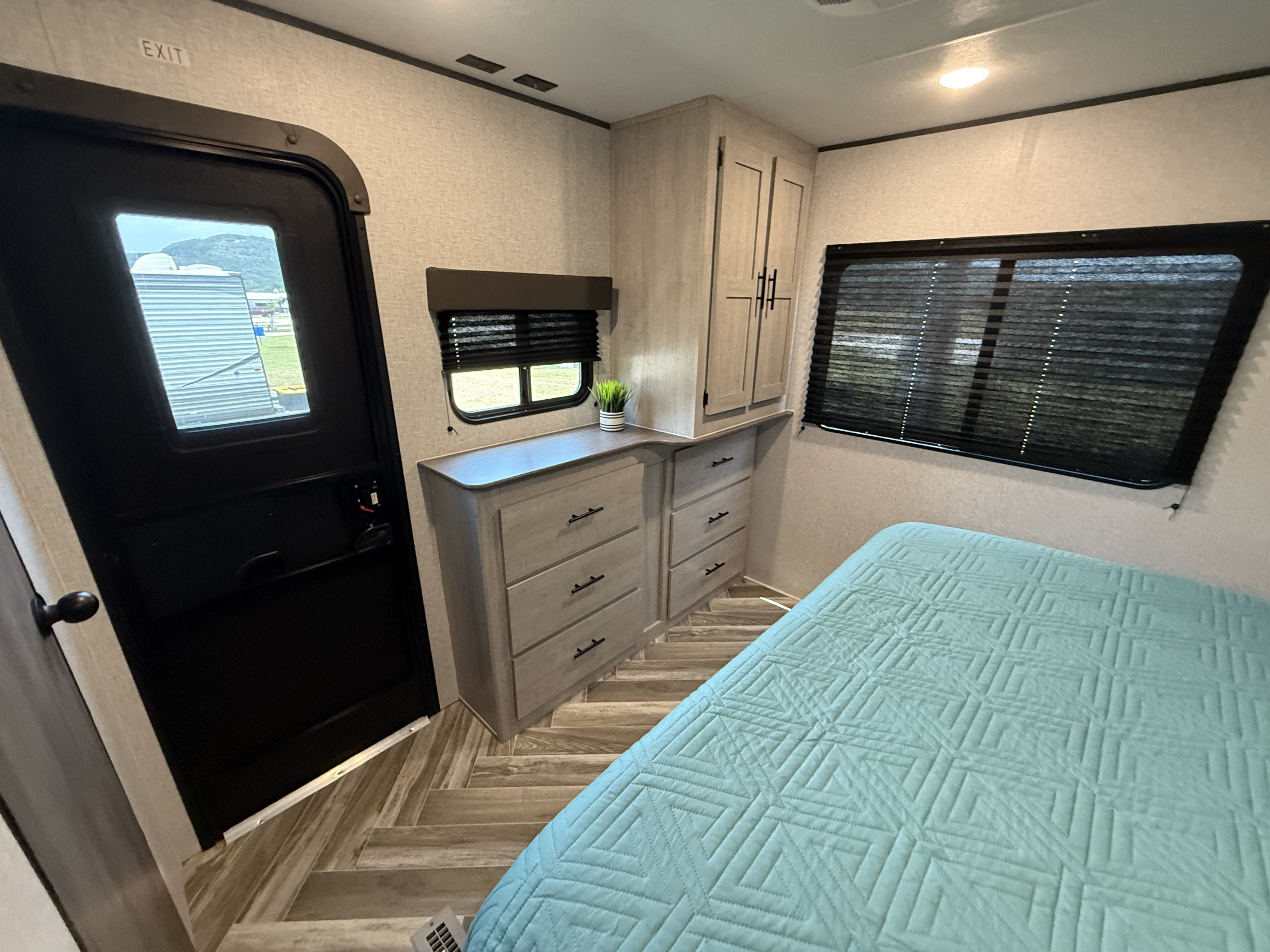 Inside an RV rental: a cozy bedroom with light wood cabinetry, blue quilted bed, and patterned flooring.. Heartland Zinger 320FB 2025