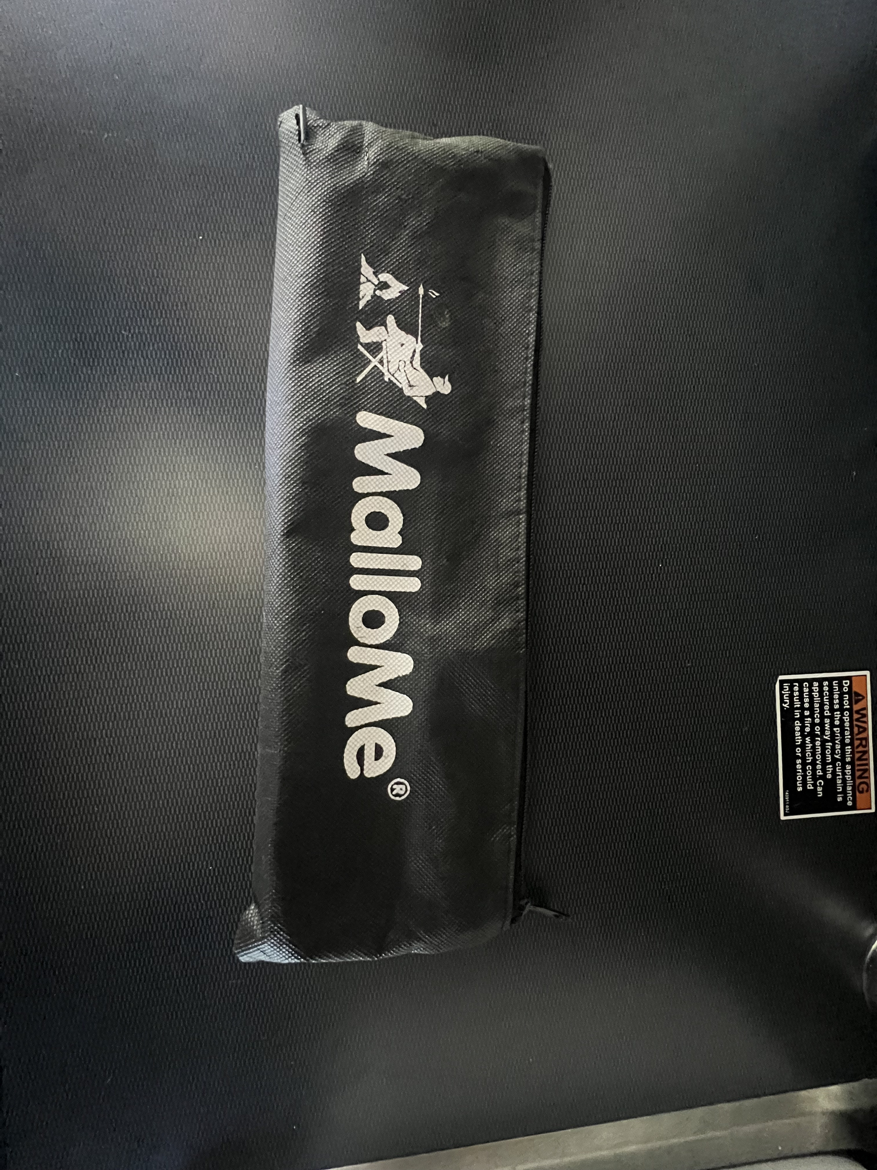 Black MalloMe camping gear bag with a marshmallow roasting logo, on a textured surface inside an rv rental. A safety warning is visible.. Winnebago Revel 2022