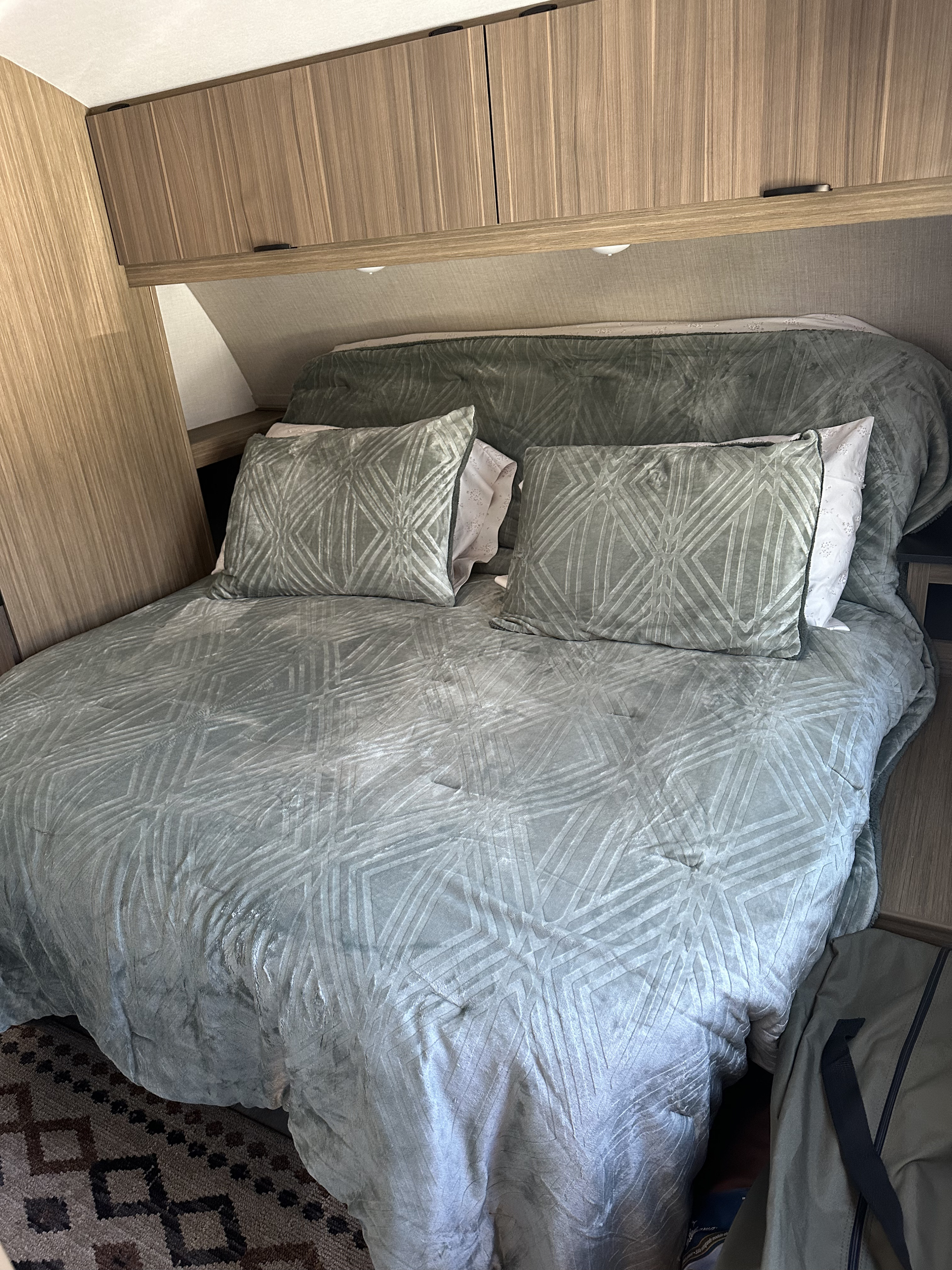 Cozy RV rental bedroom features a comfy bed with green patterned bedding, pillows, and functional overhead cabinets.. Forest River Forest River Salem Cruise Lite 263BHXL 2025