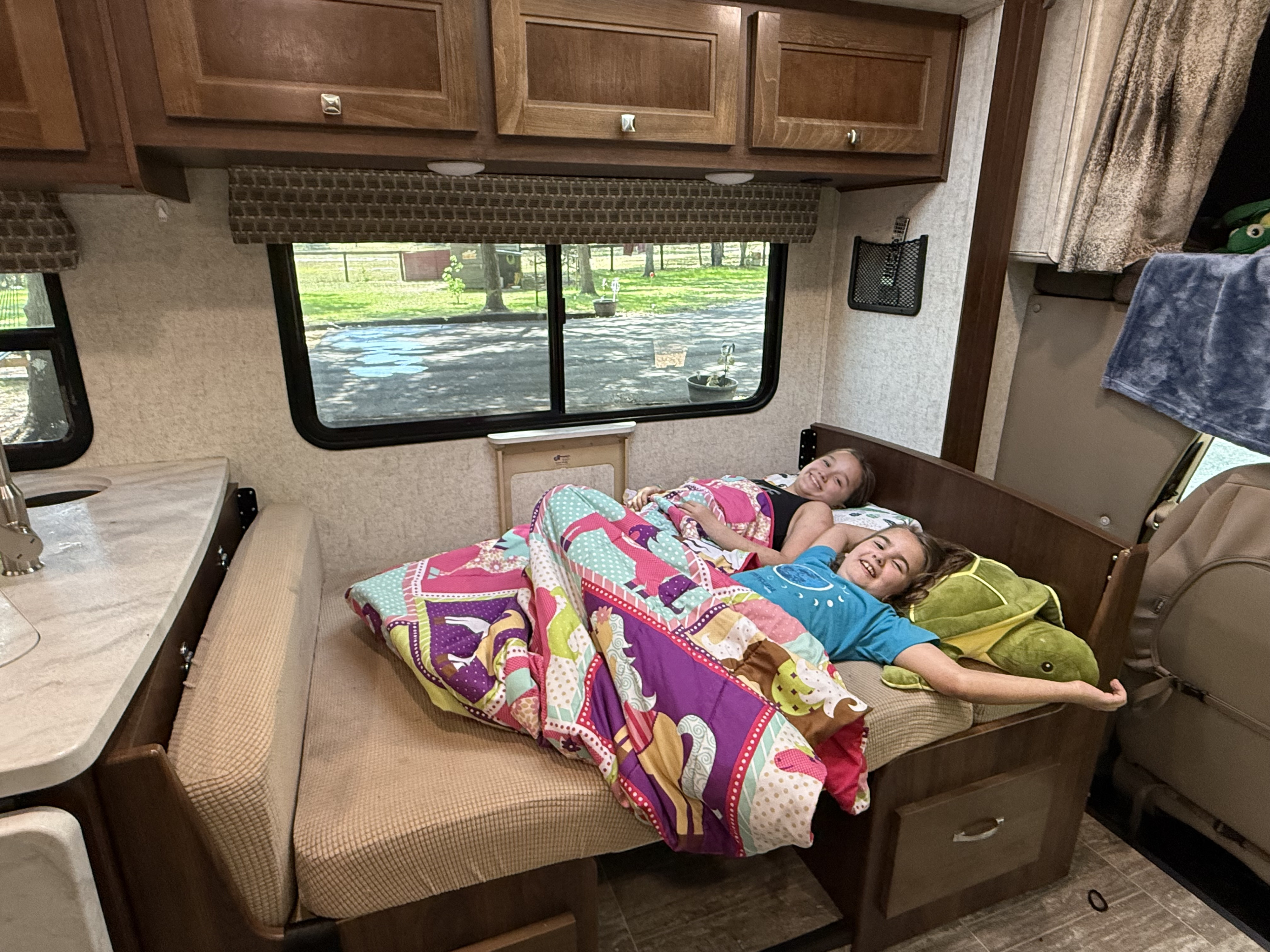 Relaxing inside their RV rental: two smiling girls with a colorful quilt.. Forest River Sunseeker 2020