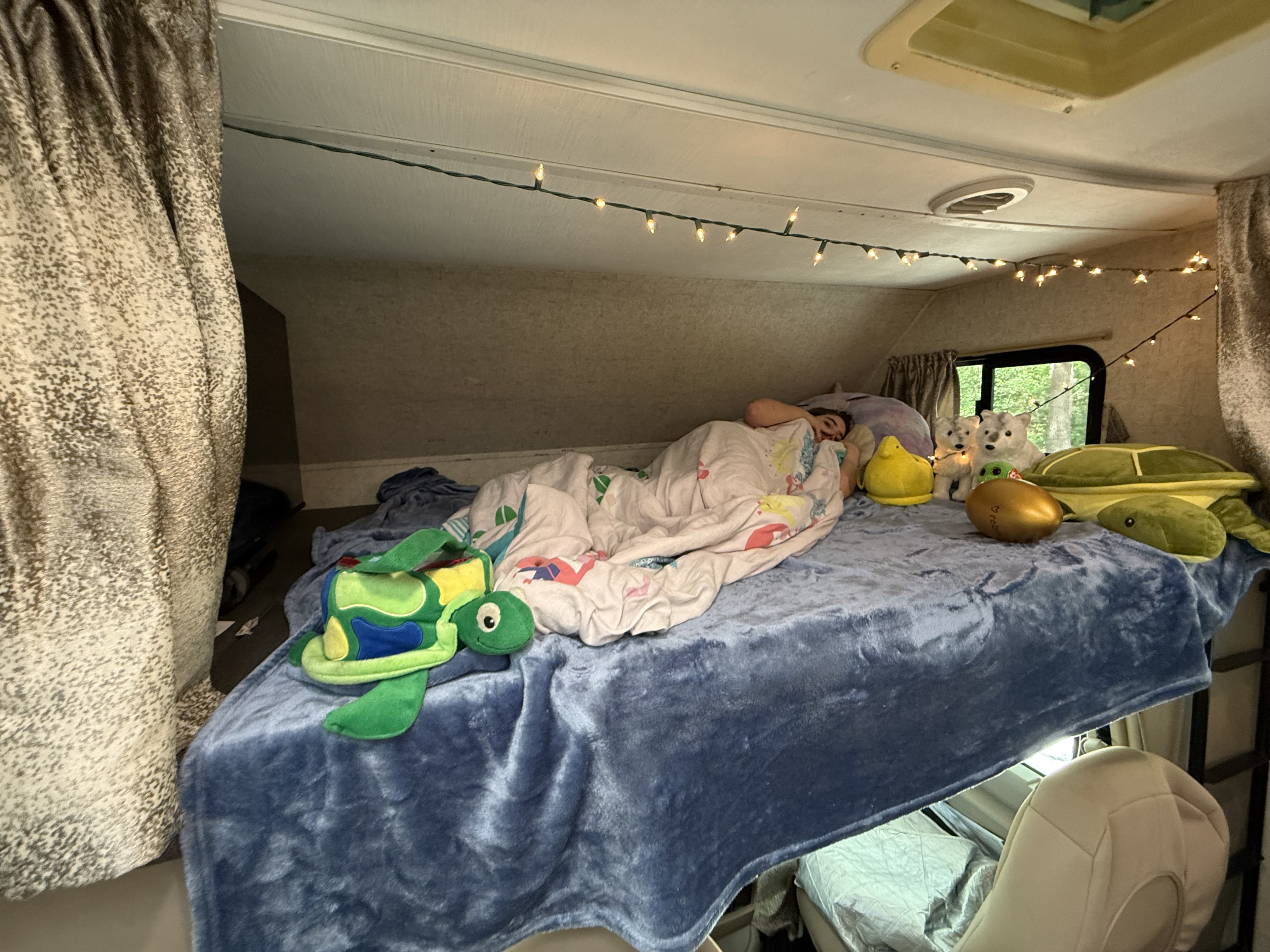 Cozy RV rental bunk with sleeping person, string lights, and stuffed animal friends. Perfect for camping trips!. Forest River Sunseeker 2020