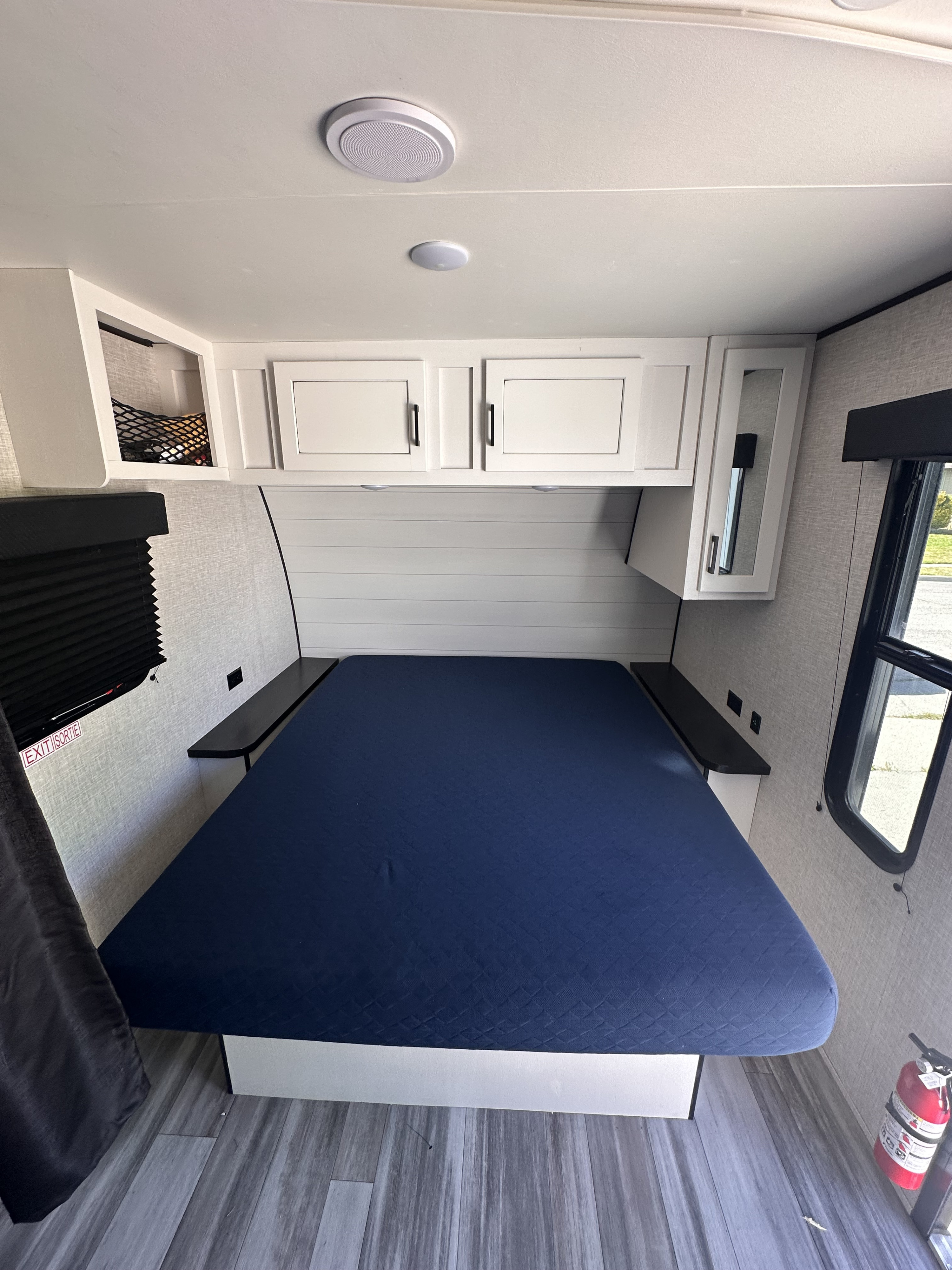 Interior view of an RV rental bedroom featuring a blue bed, white overhead cabinets, side shelves, and a window.. Jayco Jay Flight SLX 2024