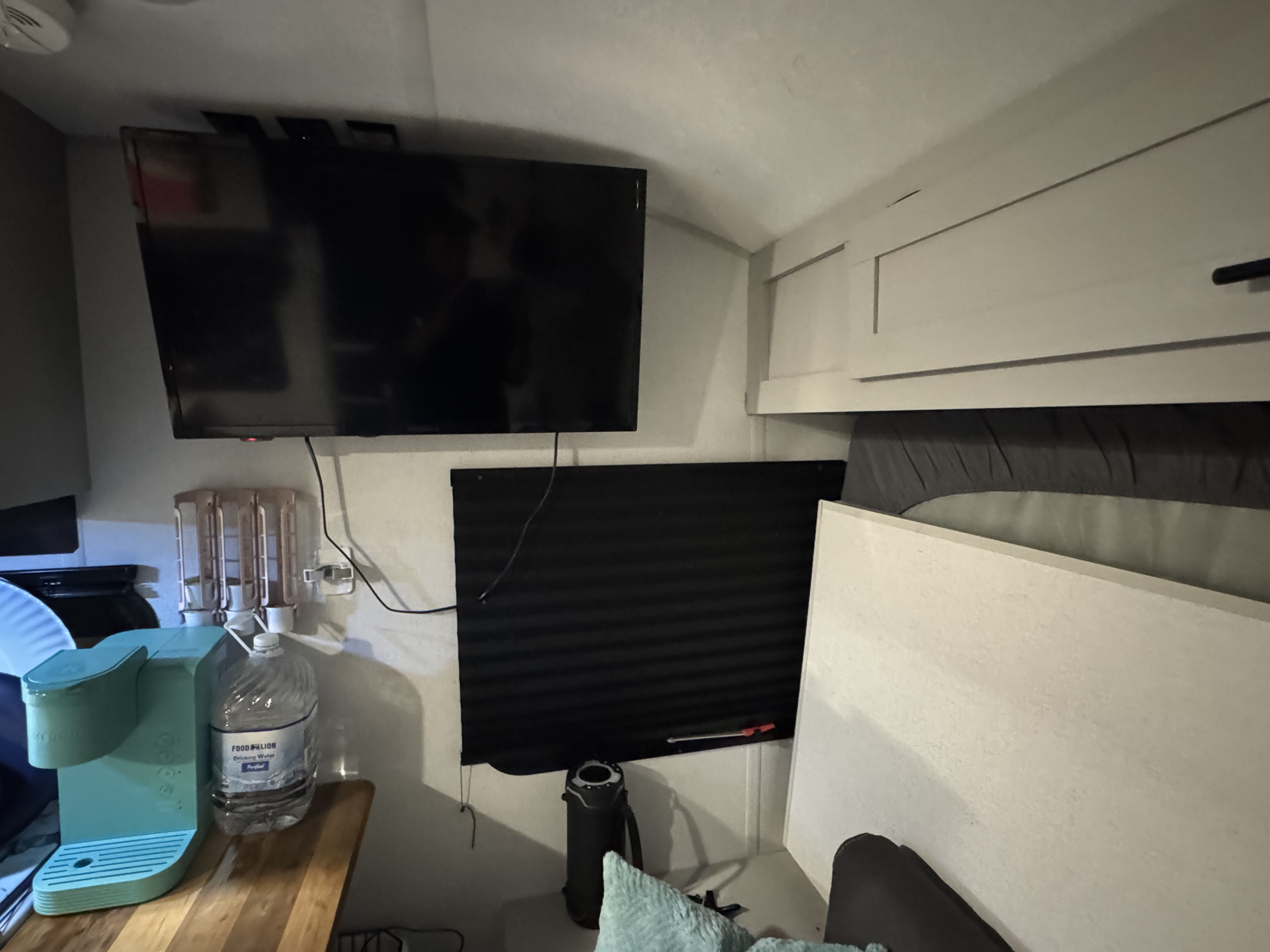 RV rental interior: This compact living space features a wall-mounted TV, coffee maker, and window blind next to the sleeping area.. Forest River Wildwood FSX 2021