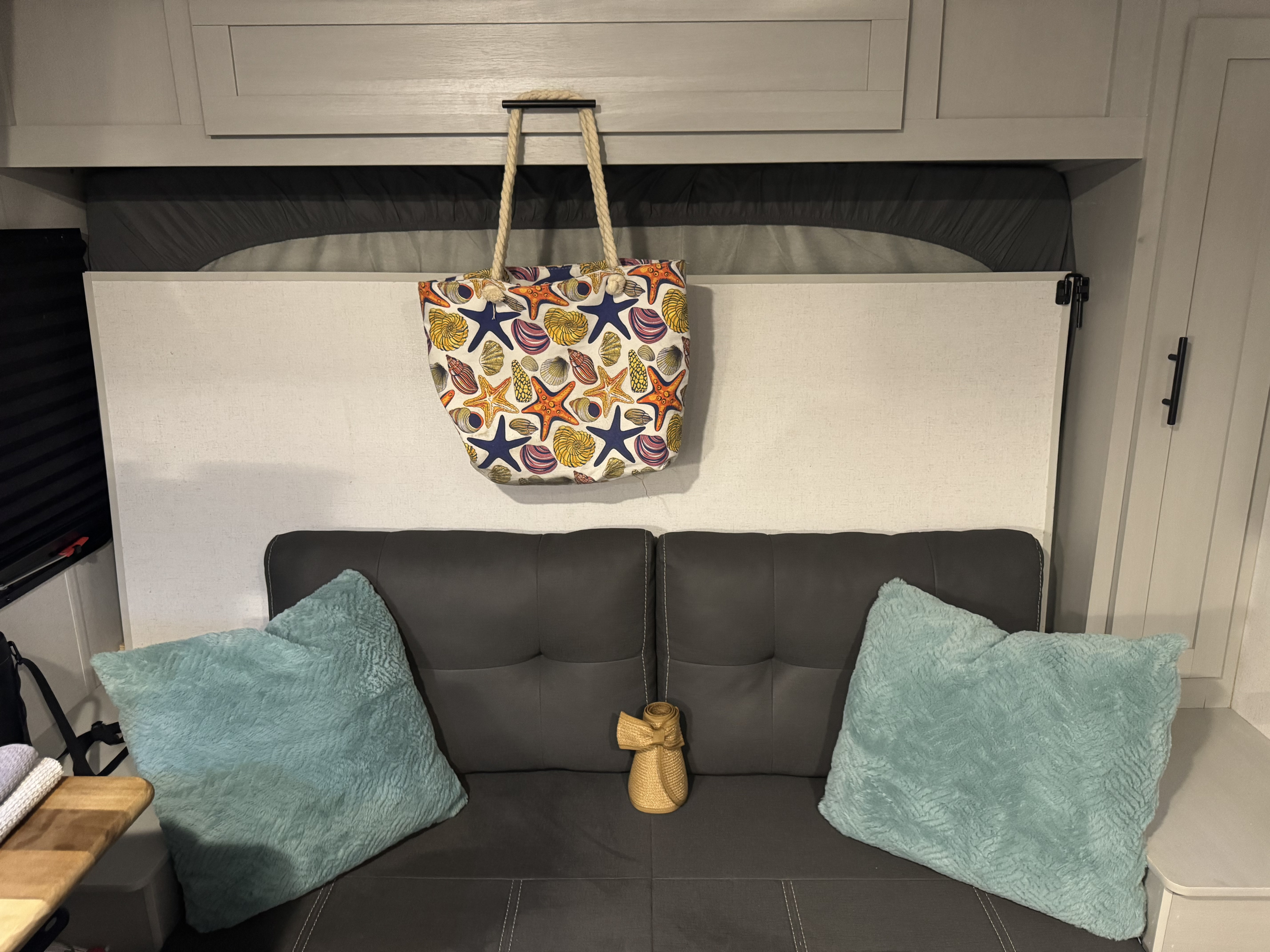 Cozy RV rental interior: gray sofa bed with aqua pillows, beach-themed tote, and hidden pull-down bed above with storage.. Forest River Wildwood FSX 2021