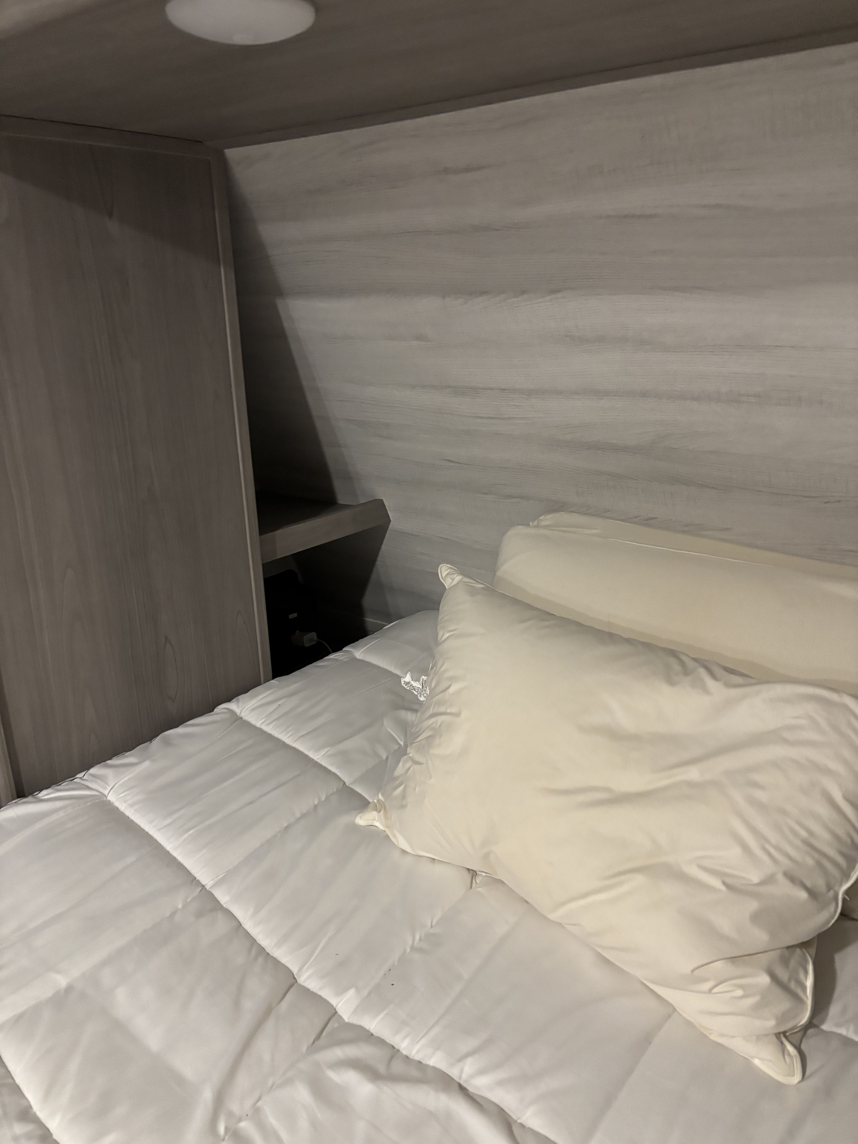 Compact RV rental bedroom interior with a comfortable bed, white linens, wood paneling, and a bedside shelf.. Dutchmen Kodiak Ultra Lite 2023