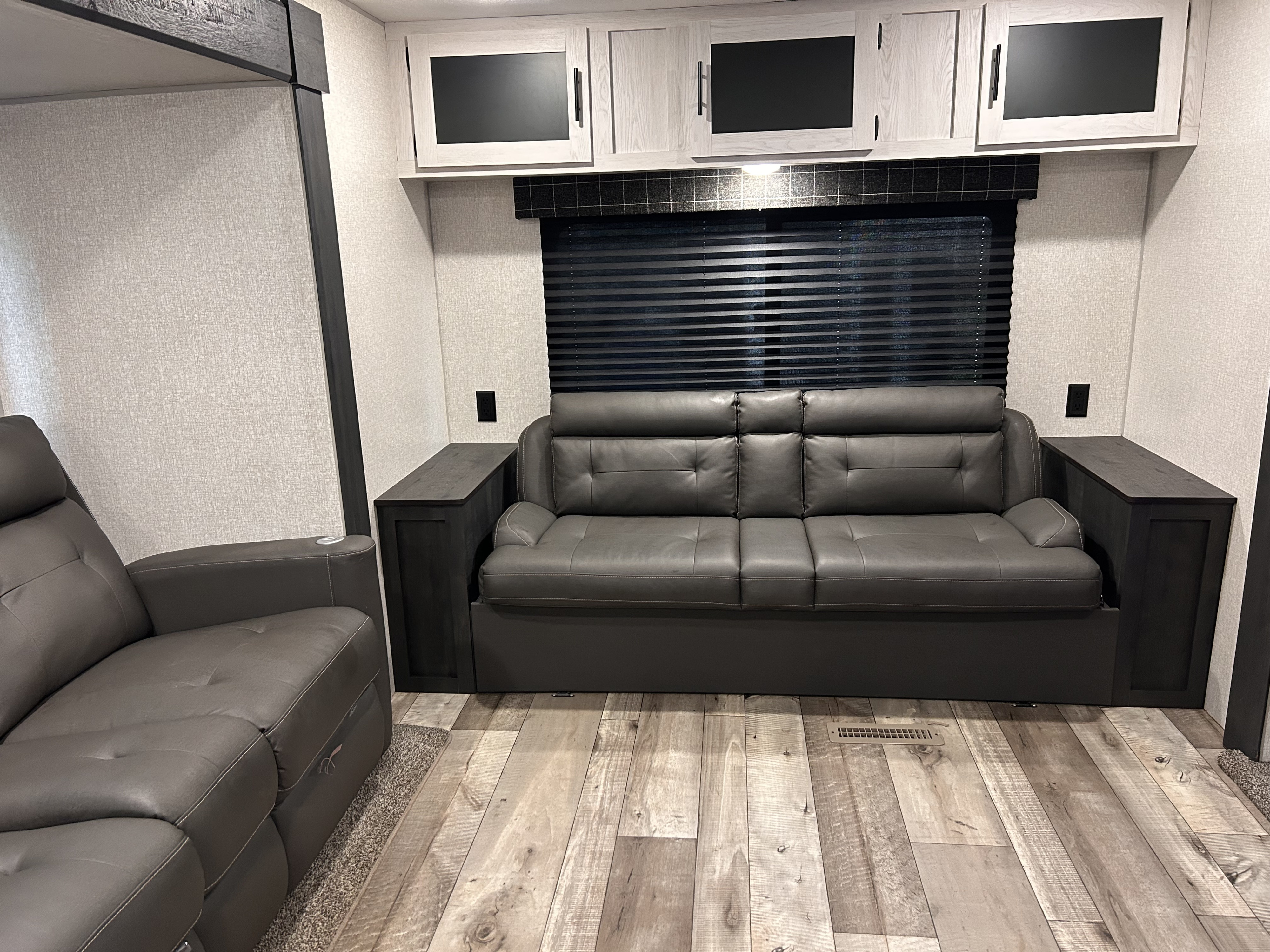 RV rental living area: modern grey sleeper sofa, overhead cabinets, black blinds, and light wood flooring.. Sportsmen SE 2022