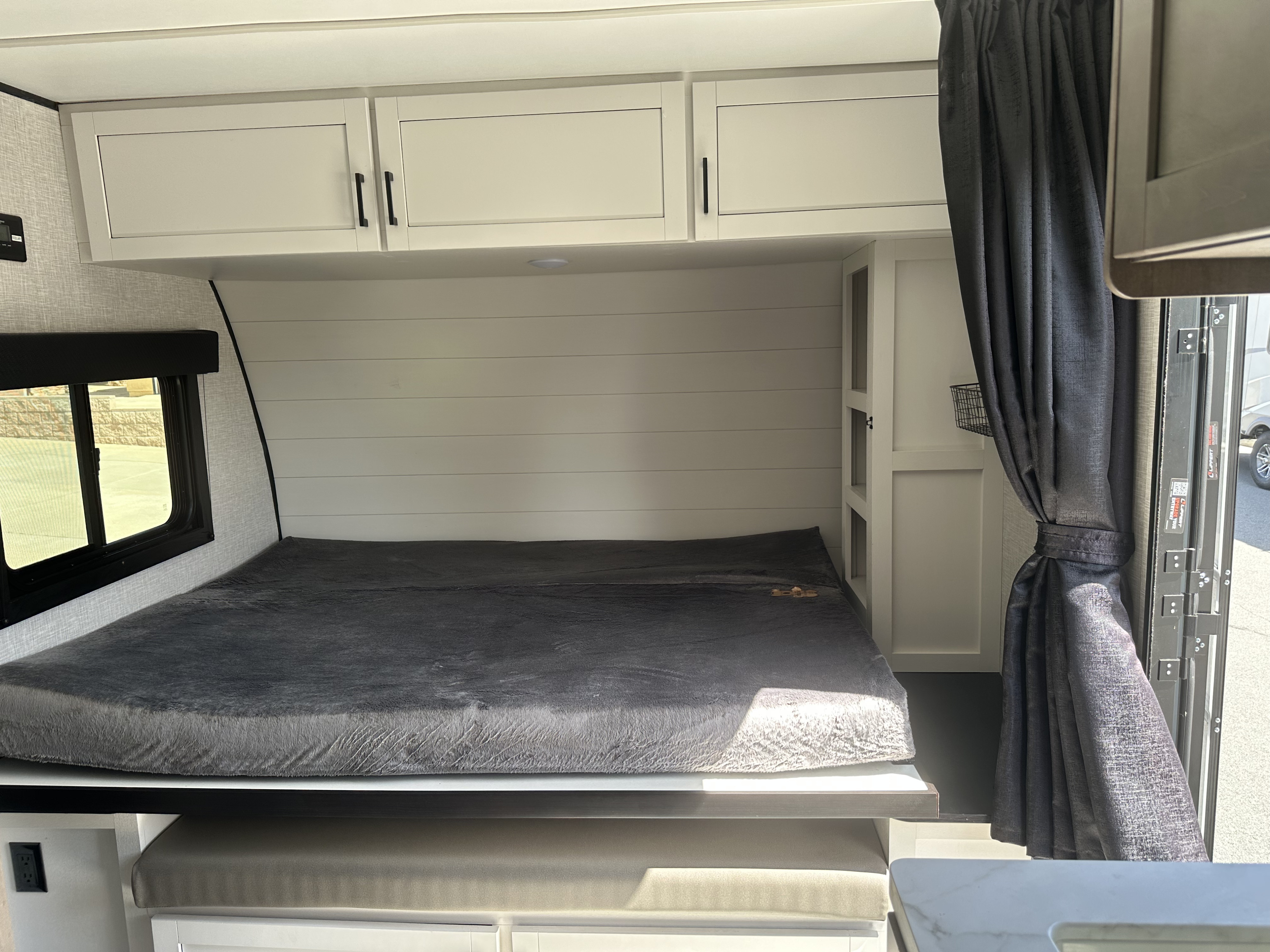RV rental bedroom view: features a dark grey bed, overhead white cabinets, a side window, and an entrance with curtains.. Autumn Ridge 188BHS 2025