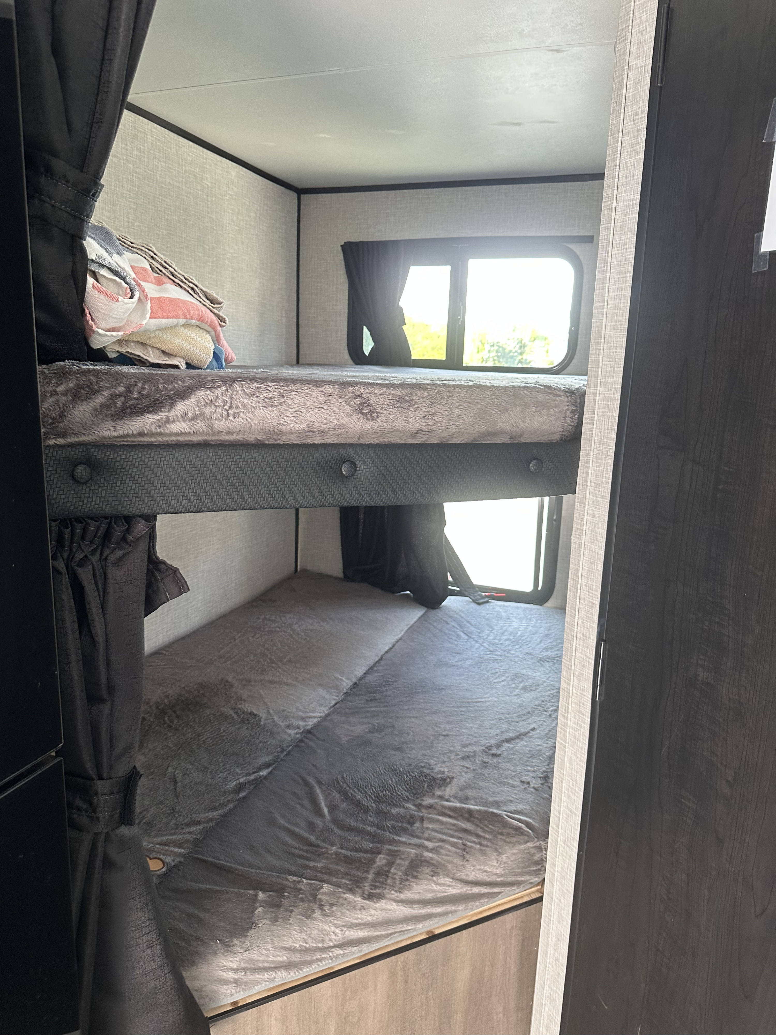 Cozy bunk beds inside an rv rental, featuring soft grey bedding and bright windows with outdoor views.. Autumn Ridge 188BHS 2025