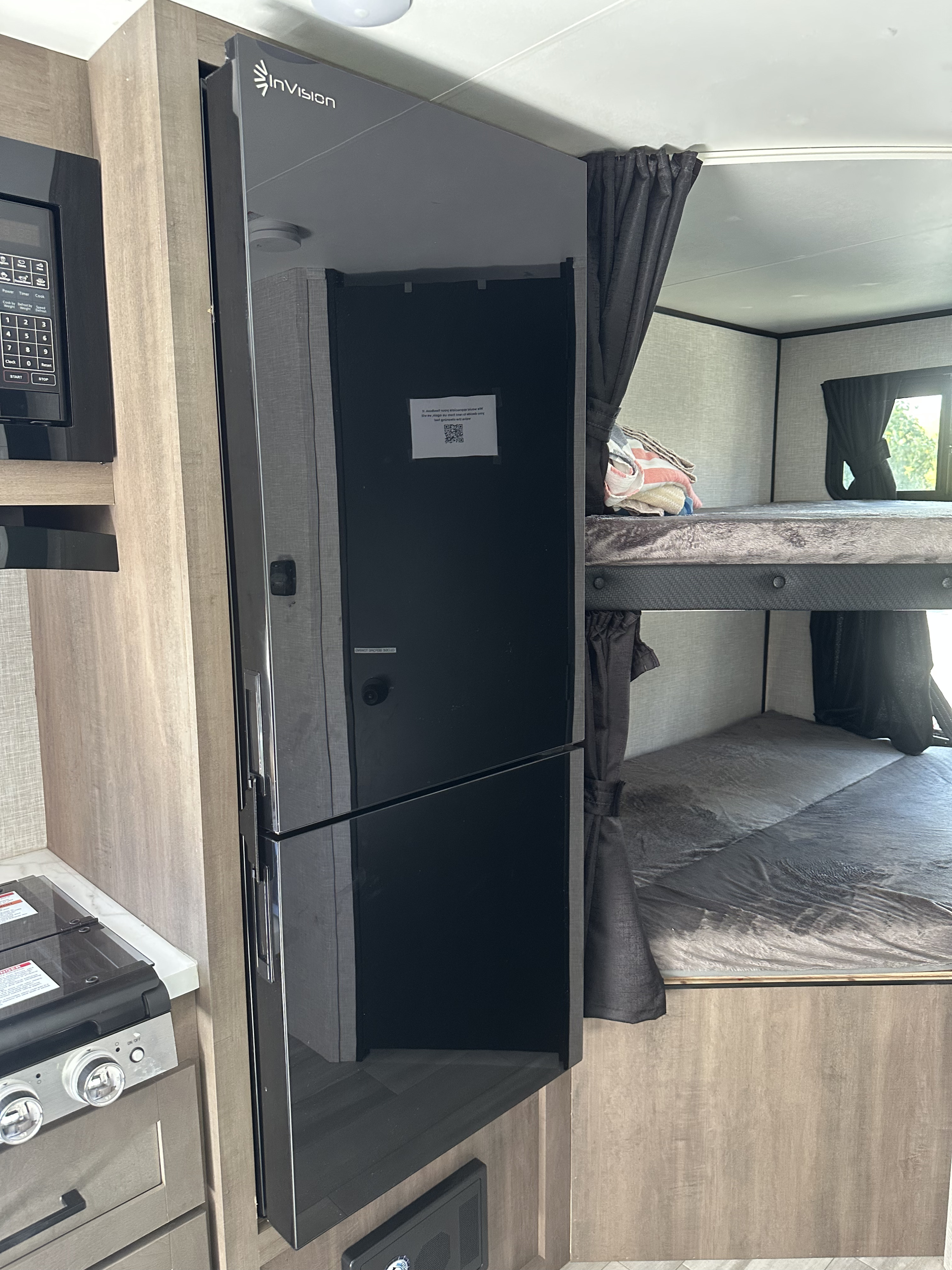 RV rental interior featuring a modern kitchen area with microwave/stove, a tall InVision refrigerator, and cozy bunk beds.. Autumn Ridge 188BHS 2025