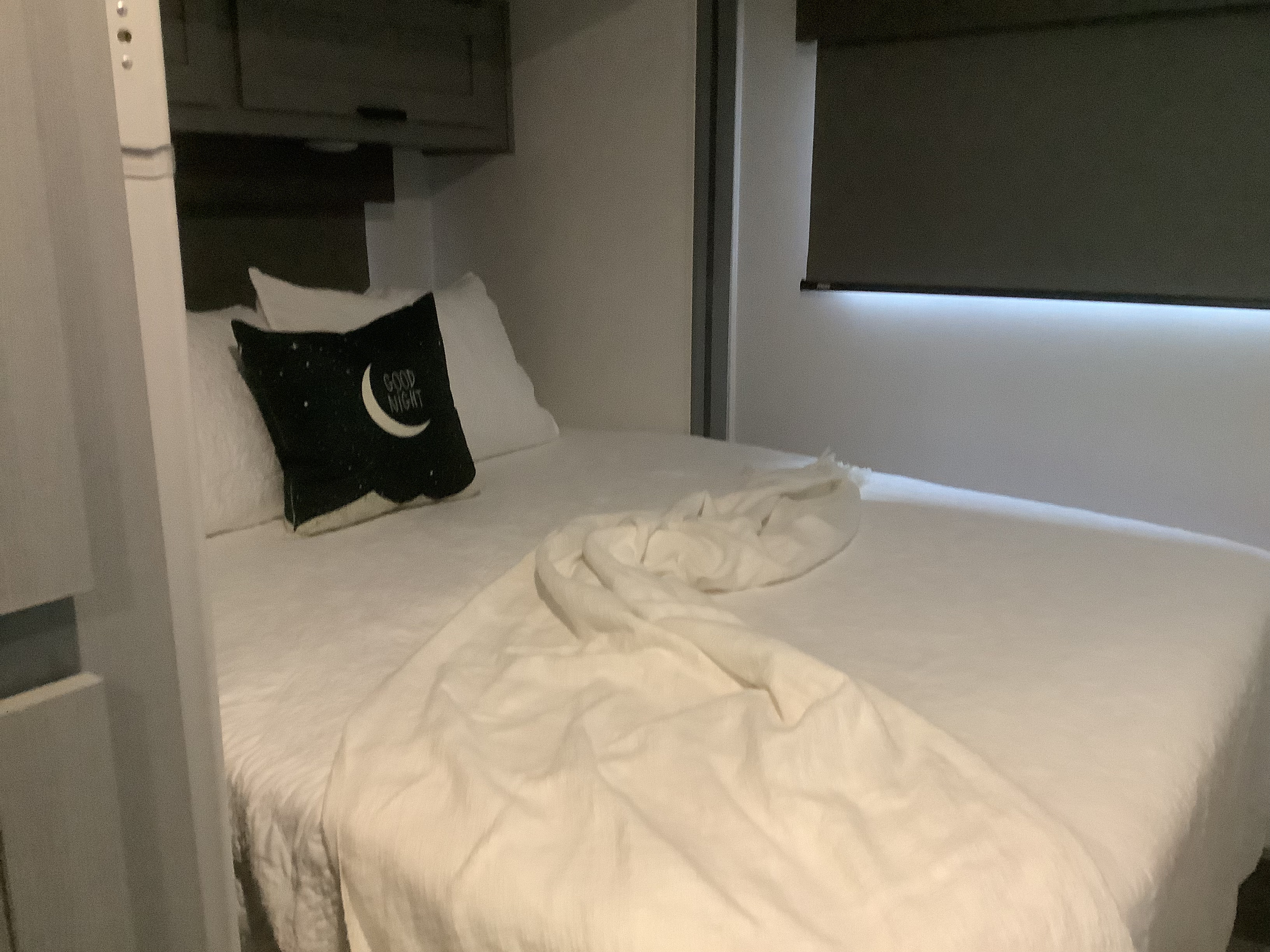 Clean RV rental bedroom with white bed, cozy "Good Night" pillow, and overhead storage. Ideal for travel.. Forest River Solera 27 DSE 2023