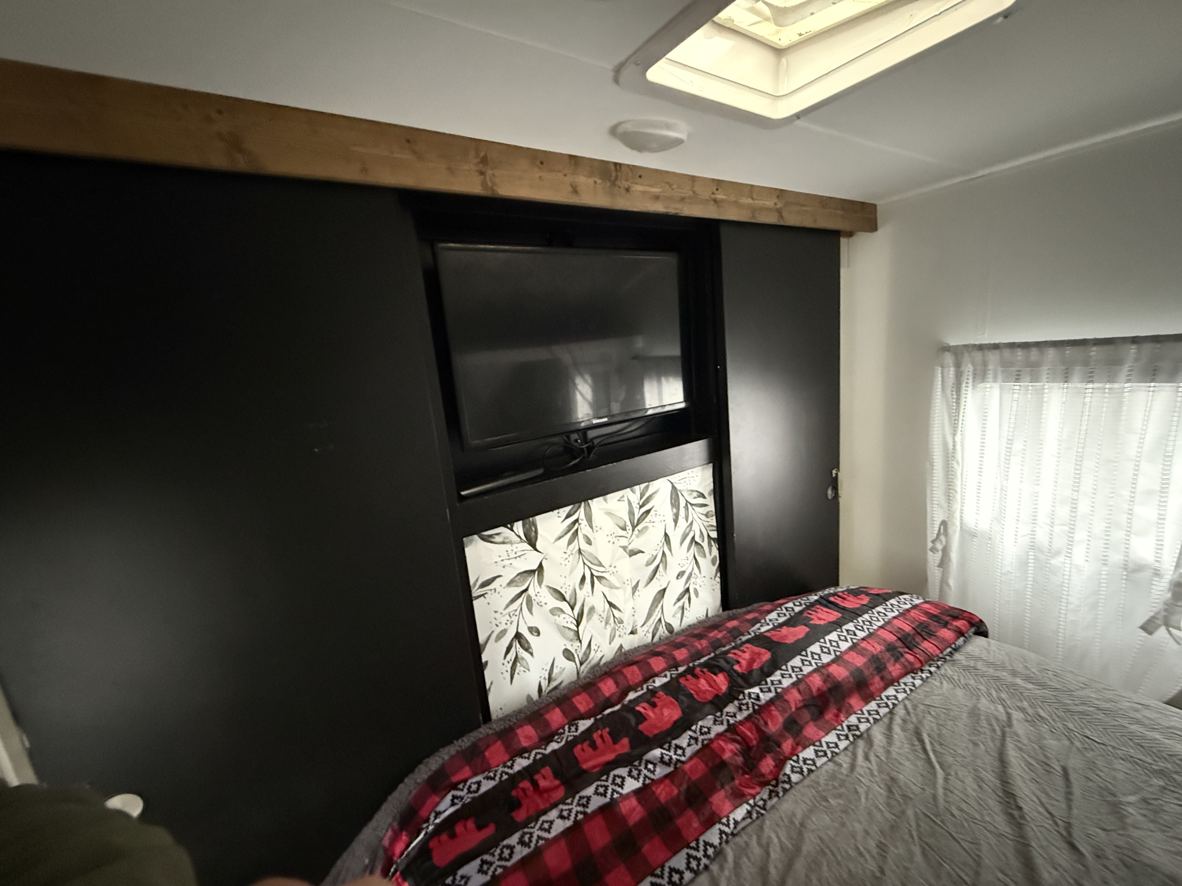 RV rental bedroom: mounted TV with sliding panels, wood trim, leafy decor, plaid moose blanket. Cozy.. Forest River Cruise lite 2017