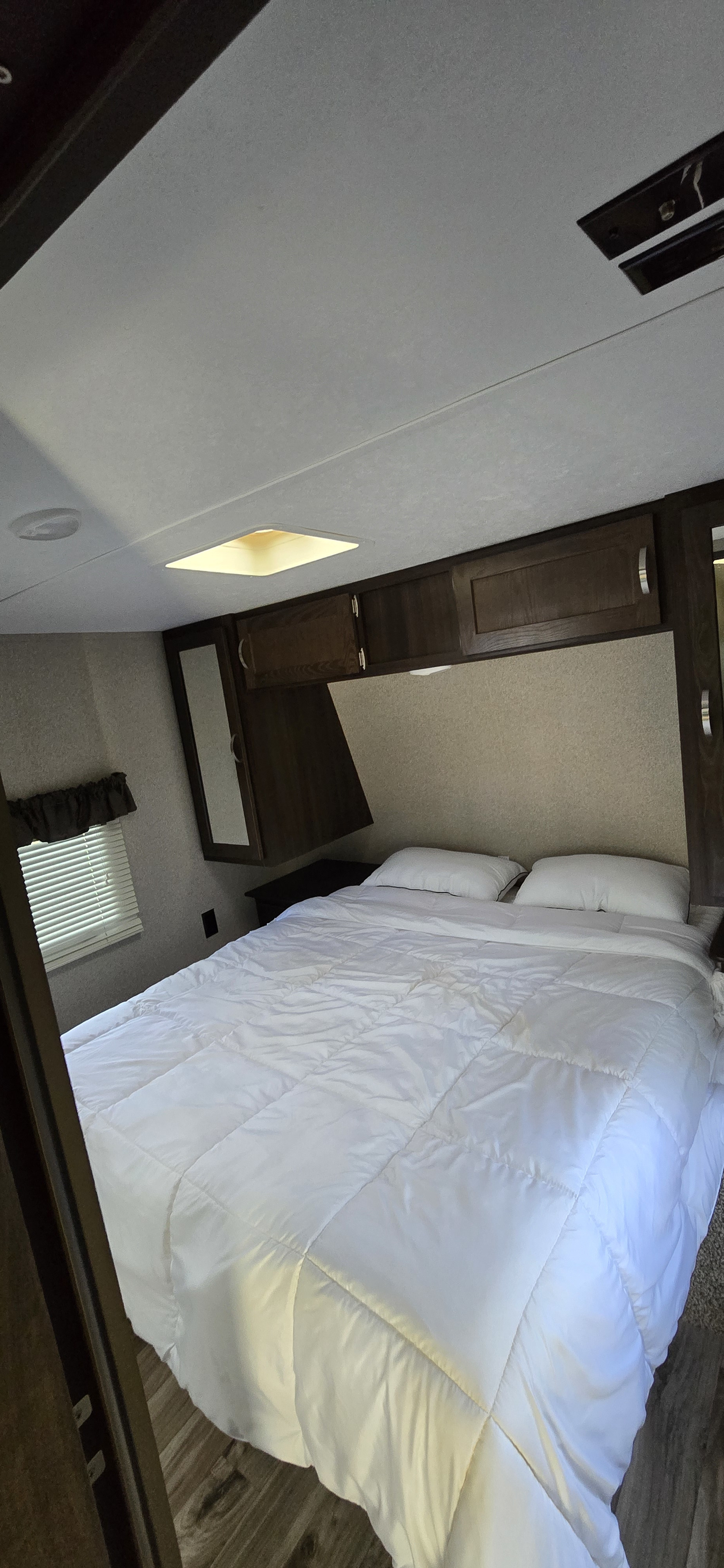 Cozy RV rental bedroom featuring a white bed, overhead storage, and a small window with blinds.. Keystone RV Springdale Eco-Lite 2019