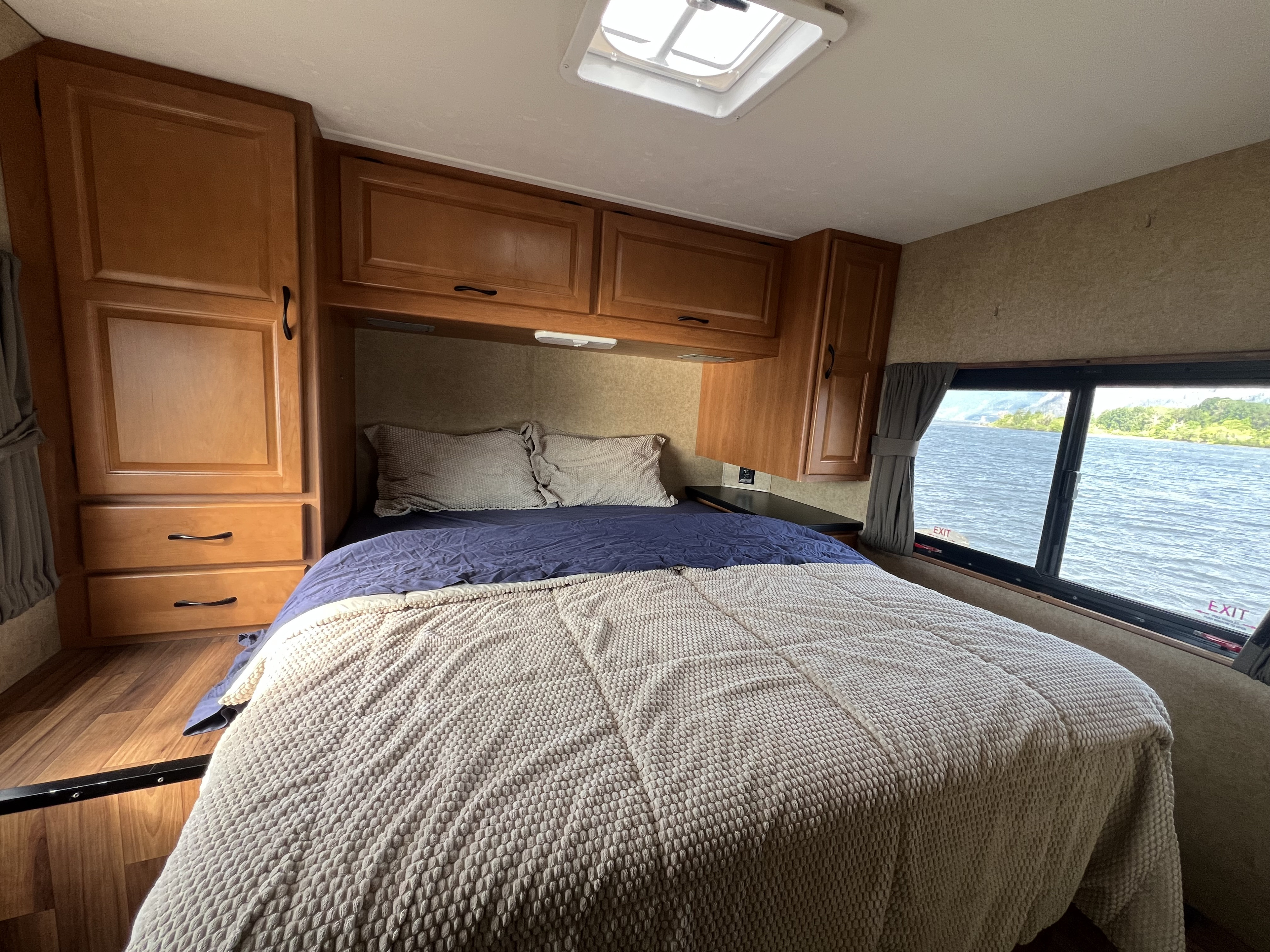 Cozy RV rental bedroom with a relaxing water view, featuring a comfortable bed, ample storage cabinets, and wood flooring.. Thor Majestic 2015