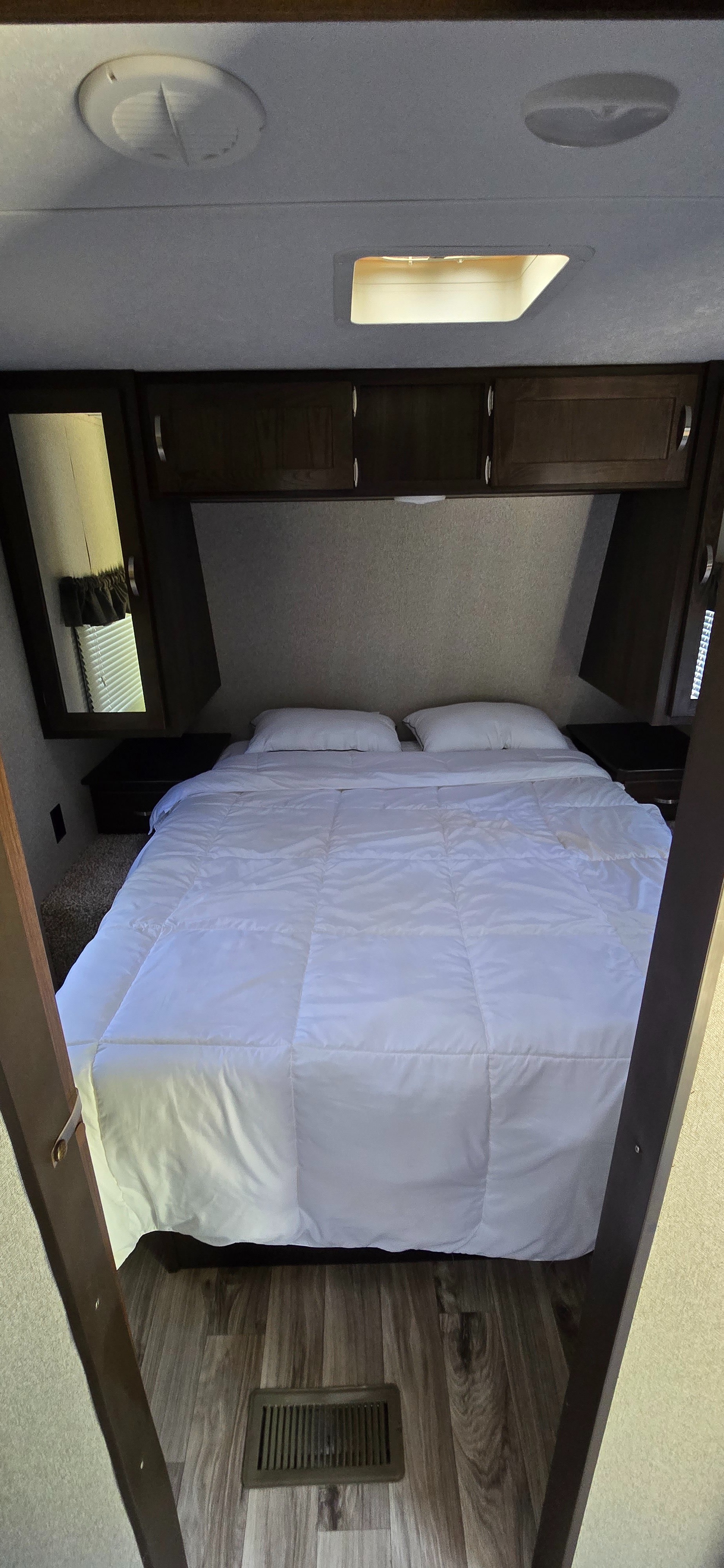 Bright RV rental bedroom: white bed, dark wood cabinets, and skylight. Compact, comfortable travel space.. Keystone RV Springdale Eco-Lite 2019