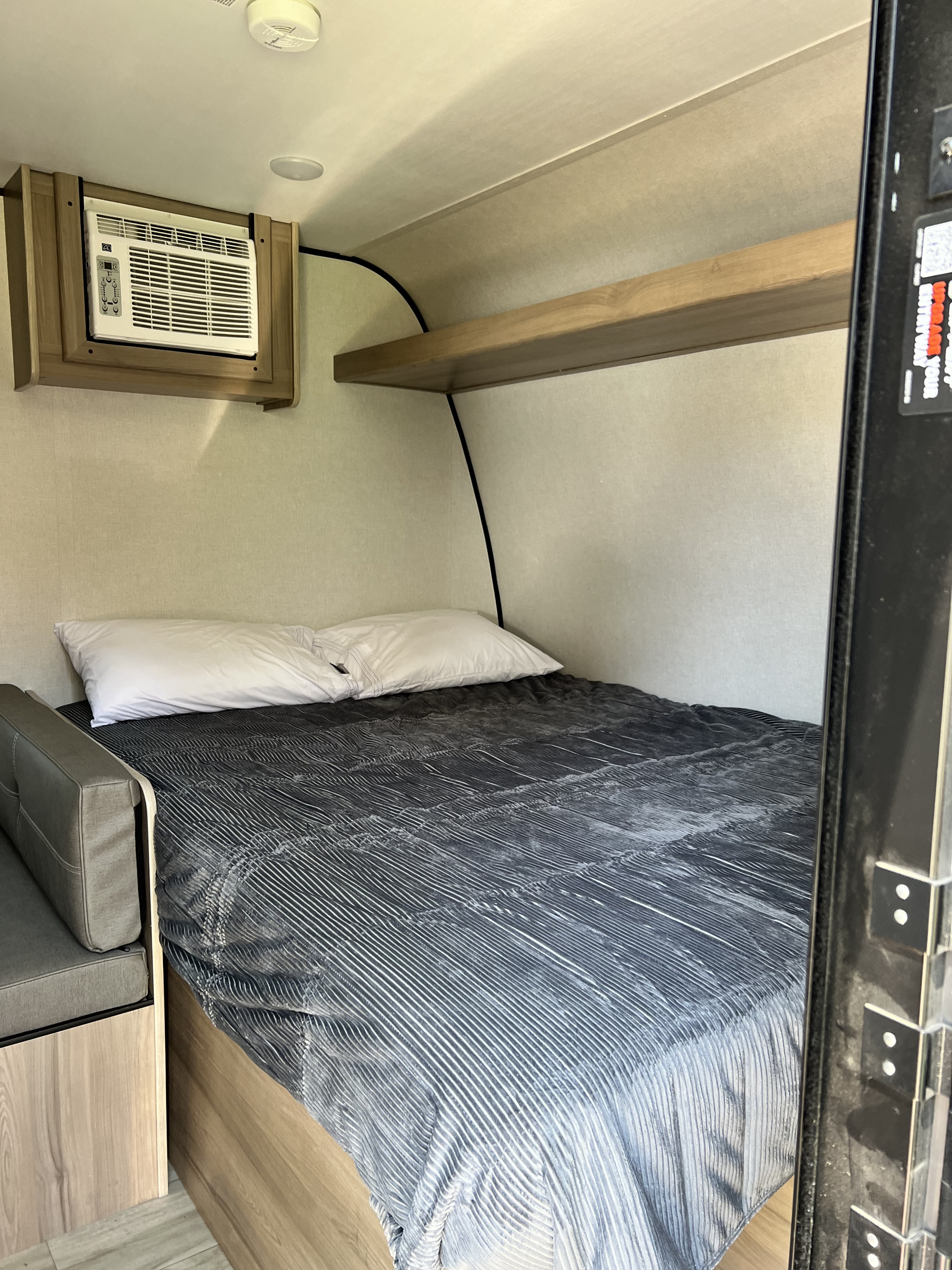 RV rental interior: a cozy sleeping area with a striped bed, pillows, an AC unit, and overhead shelf.. Coleman Lantern 17B 2025