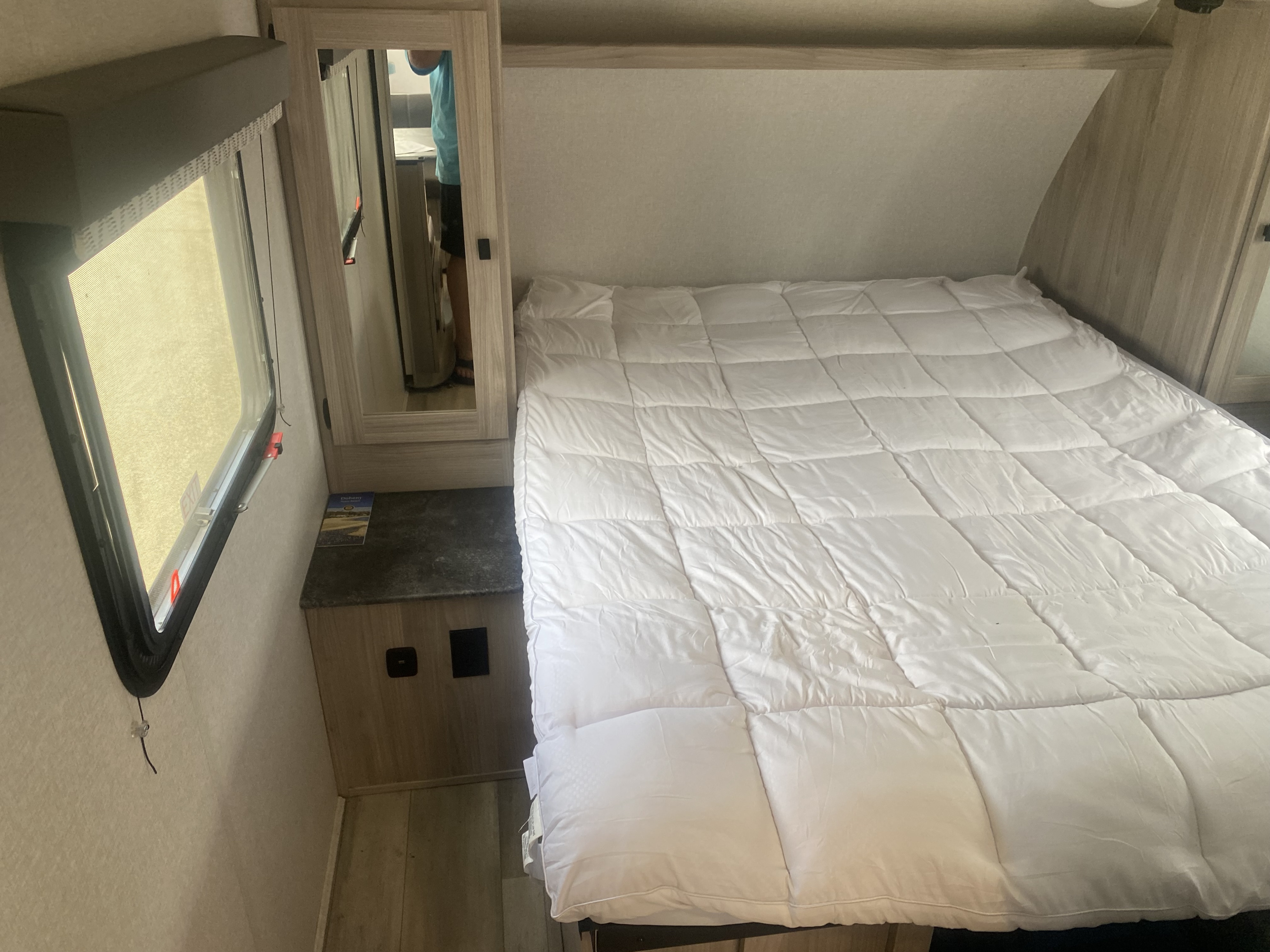 RV rental bedroom featuring a neatly made bed with white comforter, window, and bedside cabinet with mirror.. Coachmen Northern Spirit Ultra Lite 2024