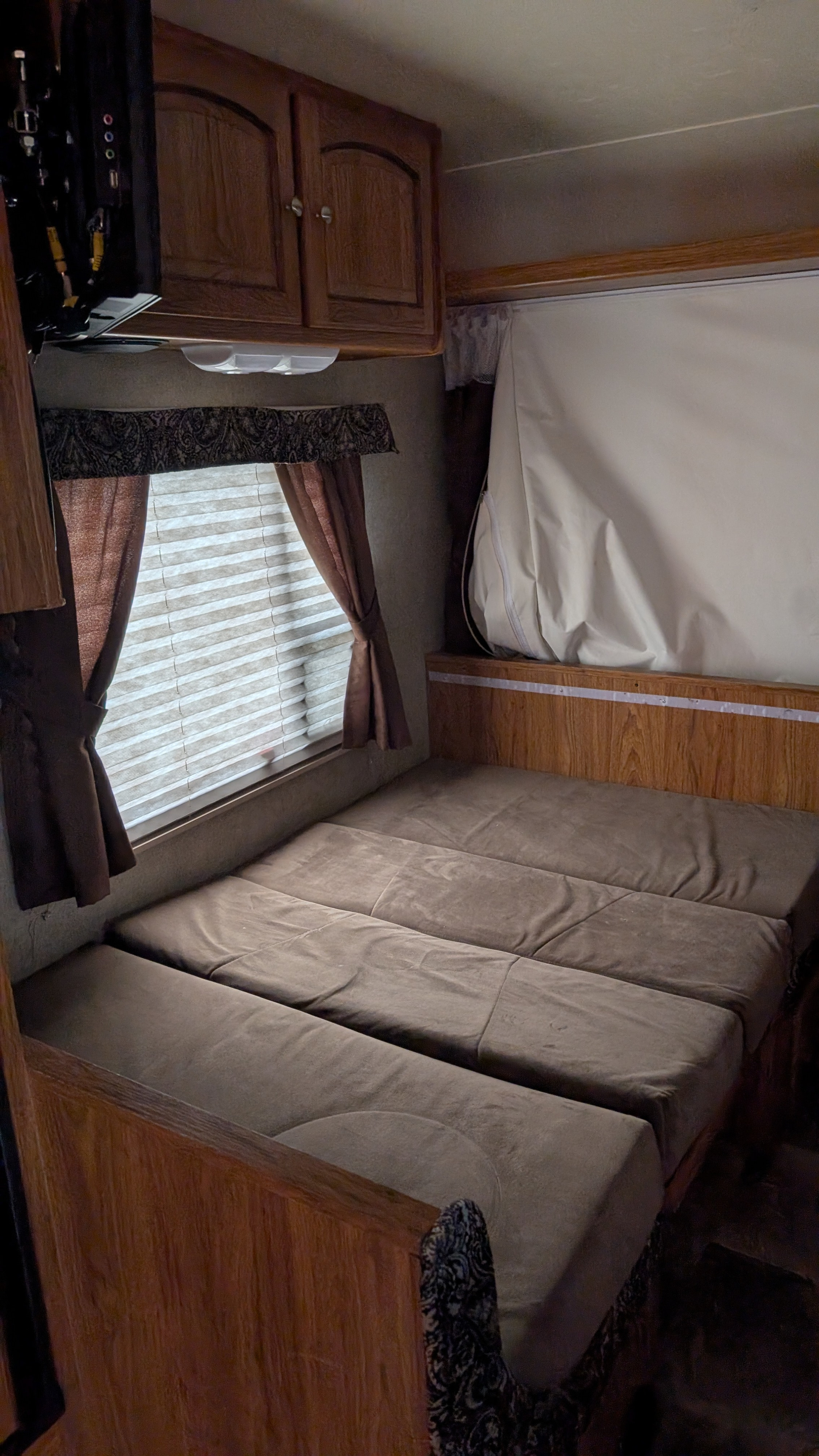 This rv rental interior features a convertible bed/dinette with brown cushions, window with blinds/curtains, wood cabinets, and a mounted TV.. Forest River ROO 2013