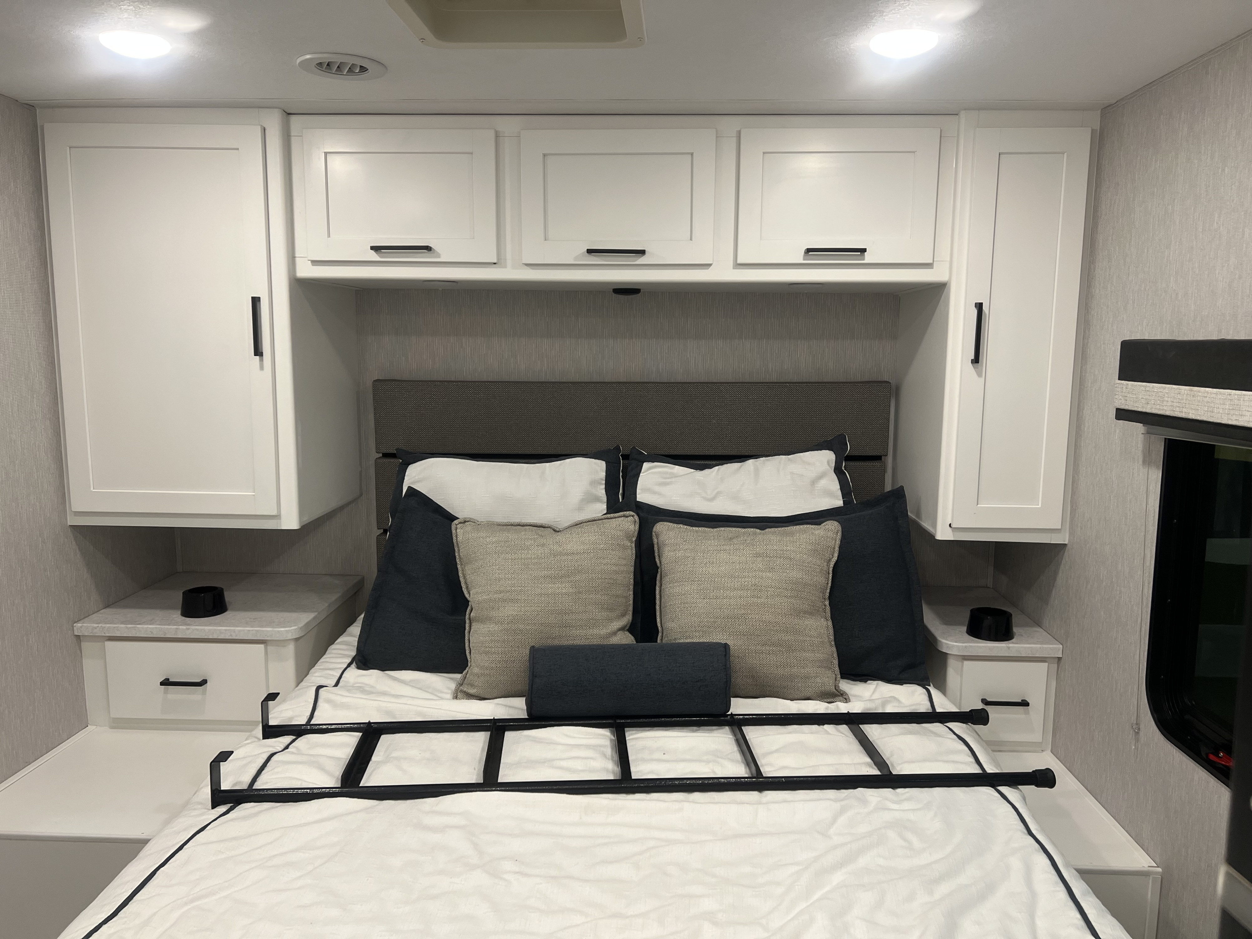 Modern RV rental bedroom: comfy bed, overhead storage, nightstands, and a bed ladder.. Forest River Coachmen Pursuit 2023