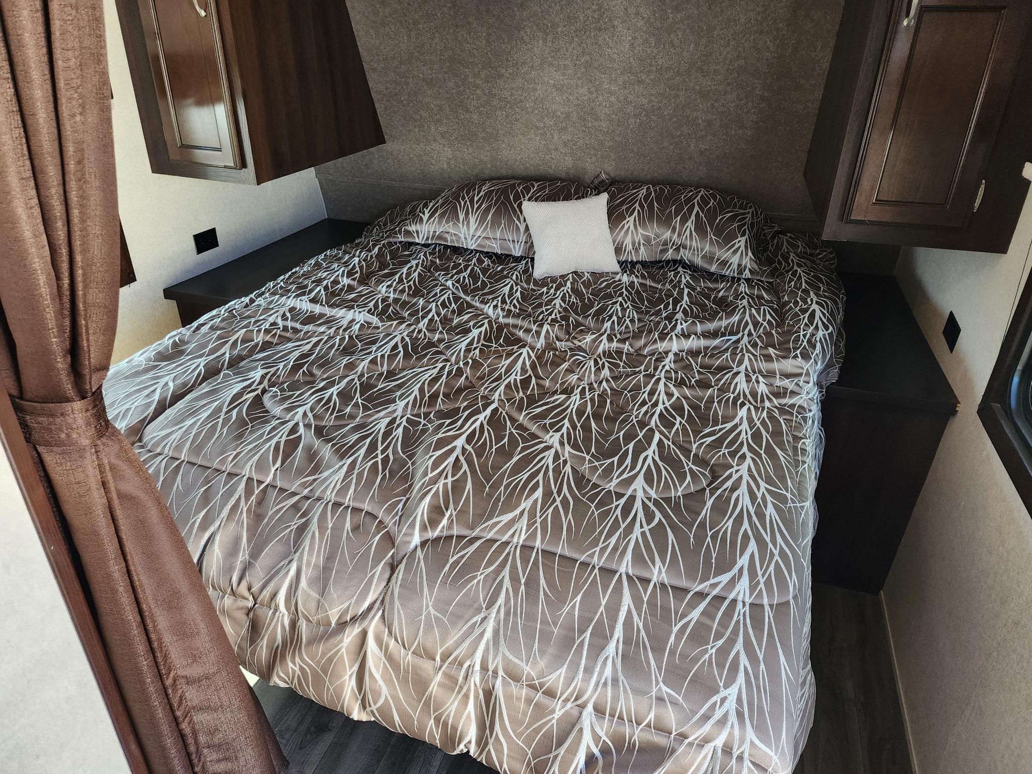 An RV rental bedroom features a comfy bed with a unique tree-branch comforter, side shelves, and overhead cabinets.. Jayco Jay Flight SLX Baja Edition 2018