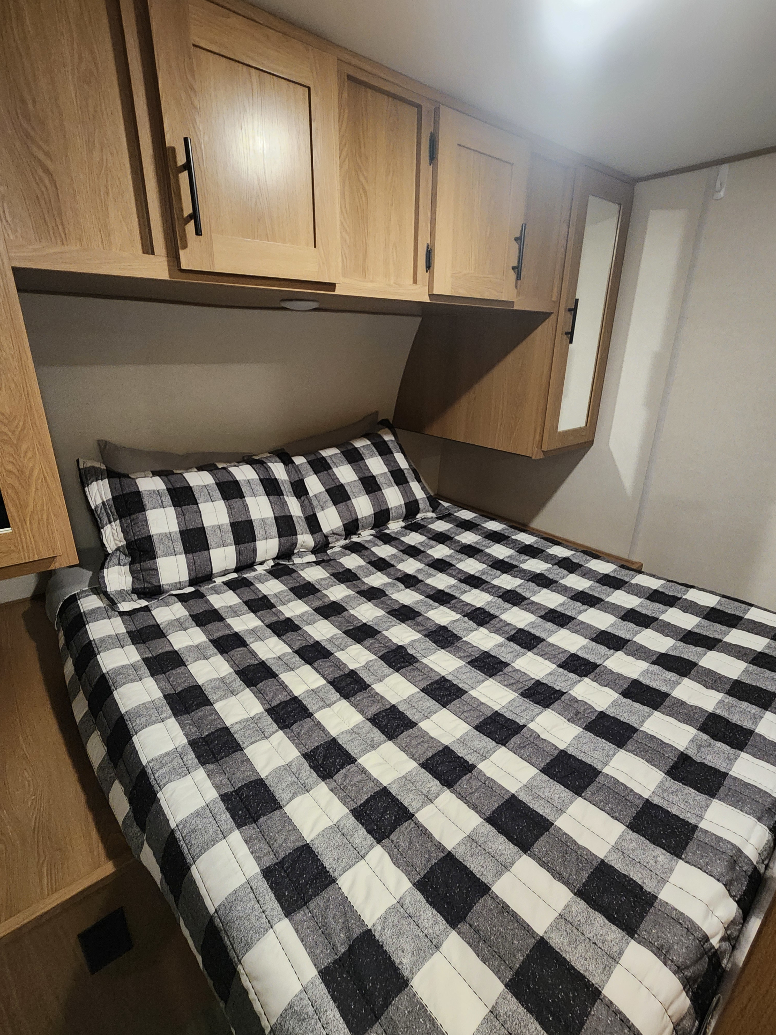 Comfortable RV rental bed with buffalo plaid bedding and overhead wooden storage cabinets.. Forest River Prime Time Avenger 24 BHS 2022