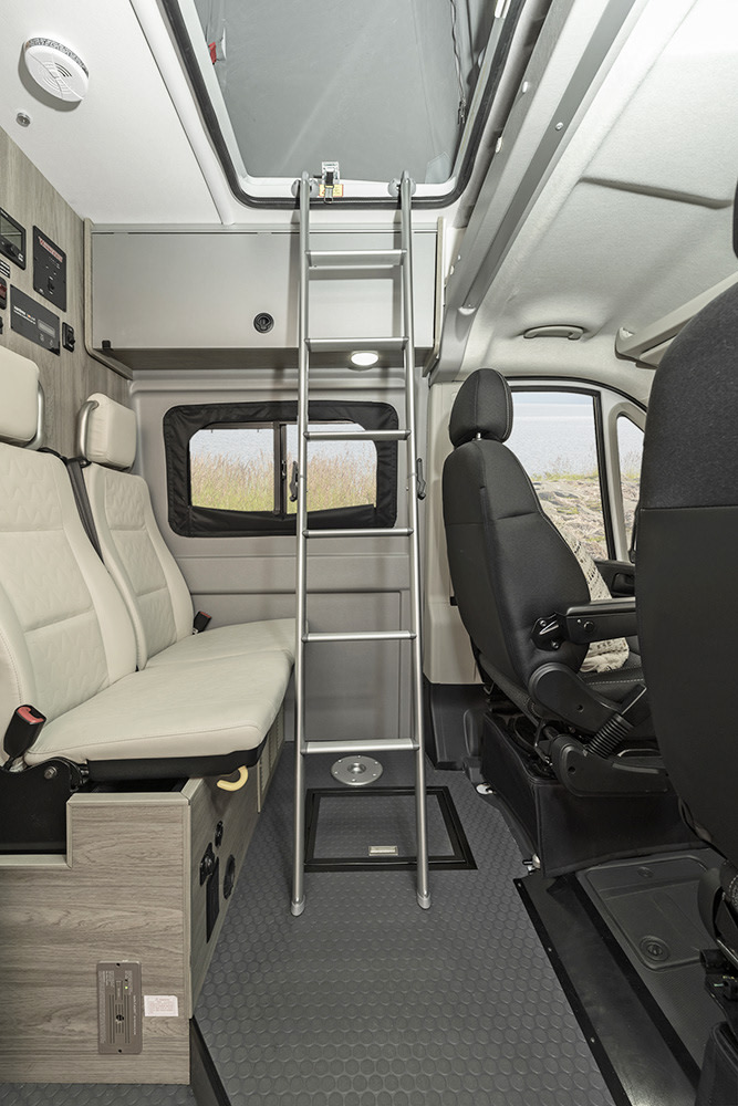 Inside an **rv rental**: a ladder leads to an overhead bunk, with bench seating & storage on the left, and the driver's area on the right.. Winnebago Solis 2023
