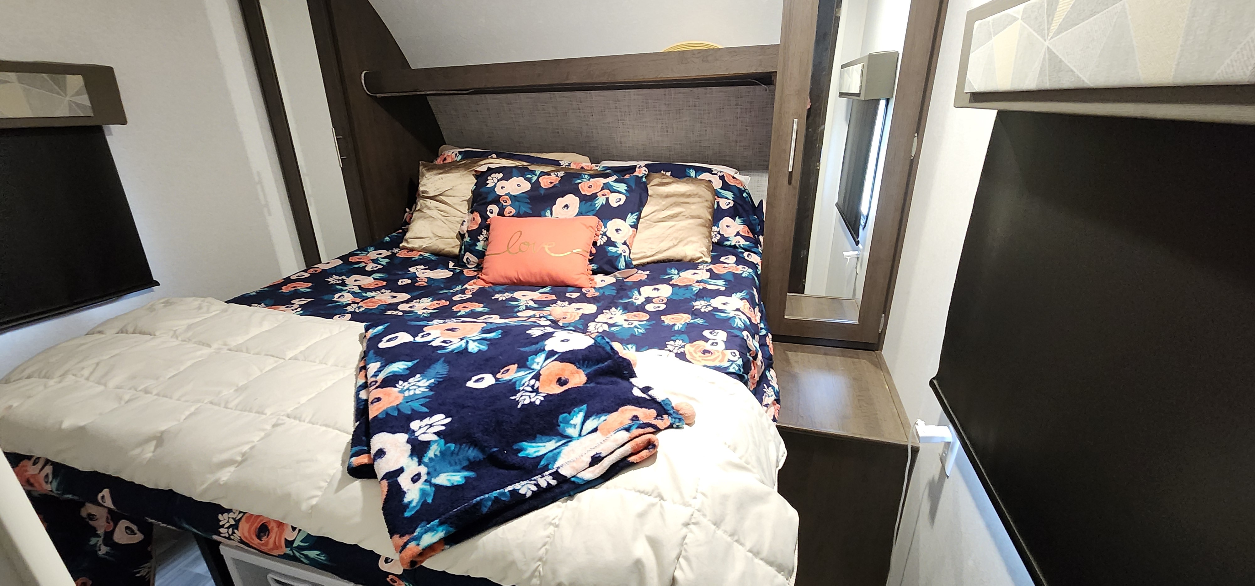 Inside a cozy RV rental: a neat bedroom with vibrant floral bedding, an orange 'love' pillow, and a mirror.. Forest River Salem 2019