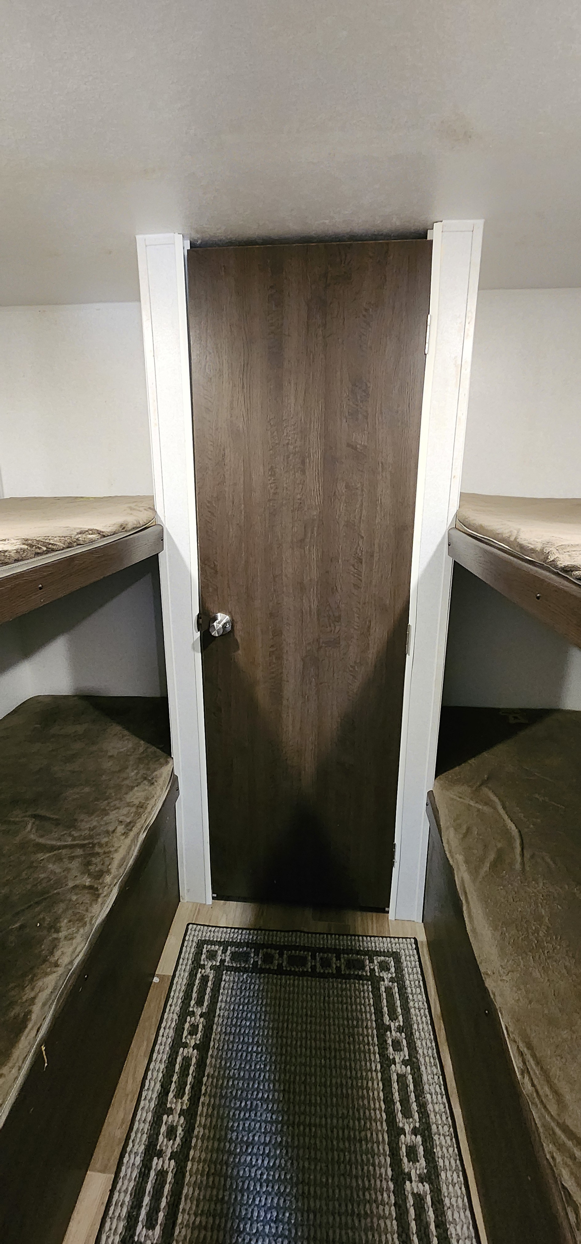 RV rental bunk room: Four compact bunk beds (two on each side) flank a central wooden door, with a patterned rug on the floor.. Forest River Salem 2019