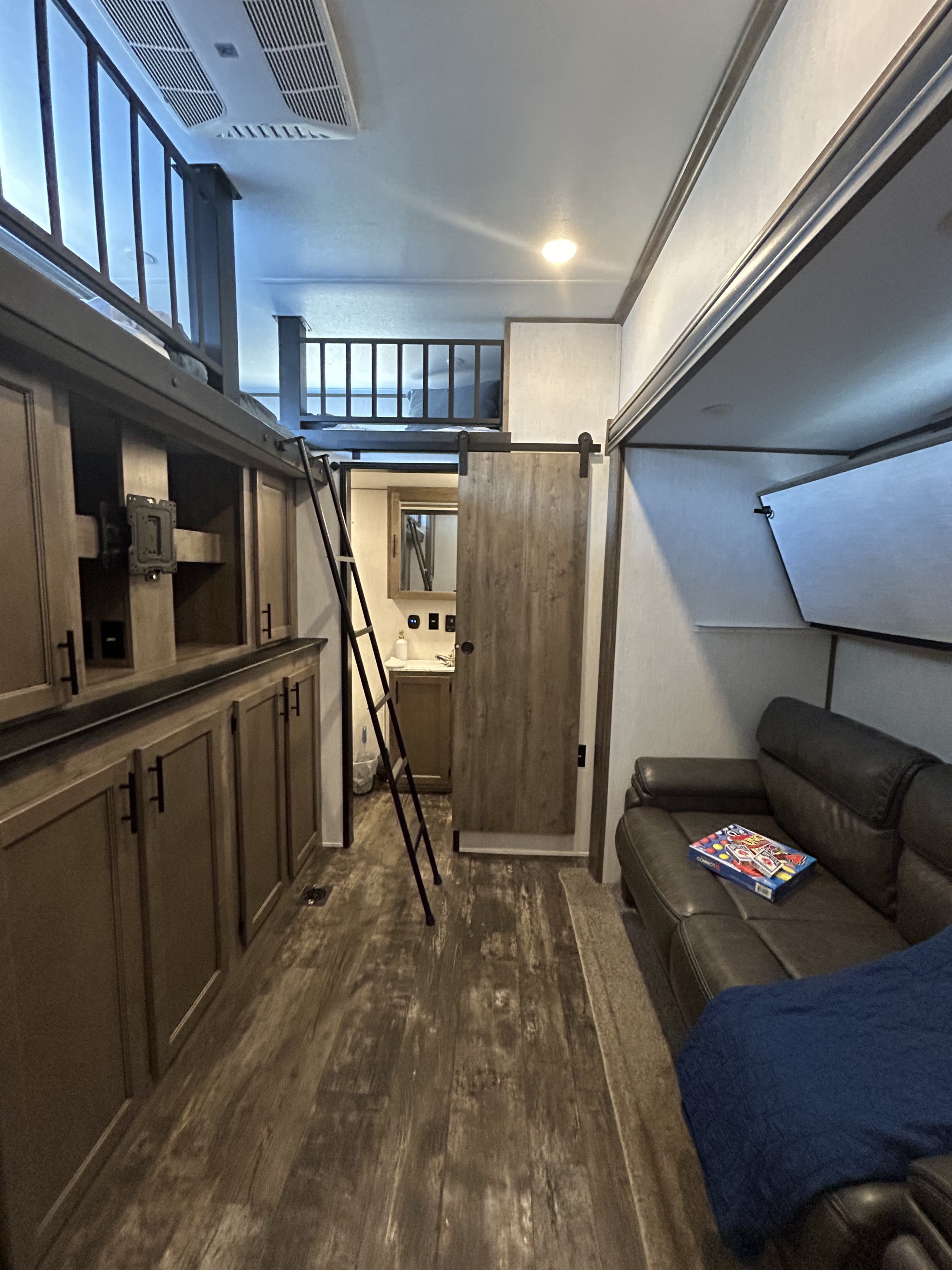 RV rental interior: living area with sofa & games, loft bunk accessed by ladder, and bathroom.. Forest River Sabre 2021