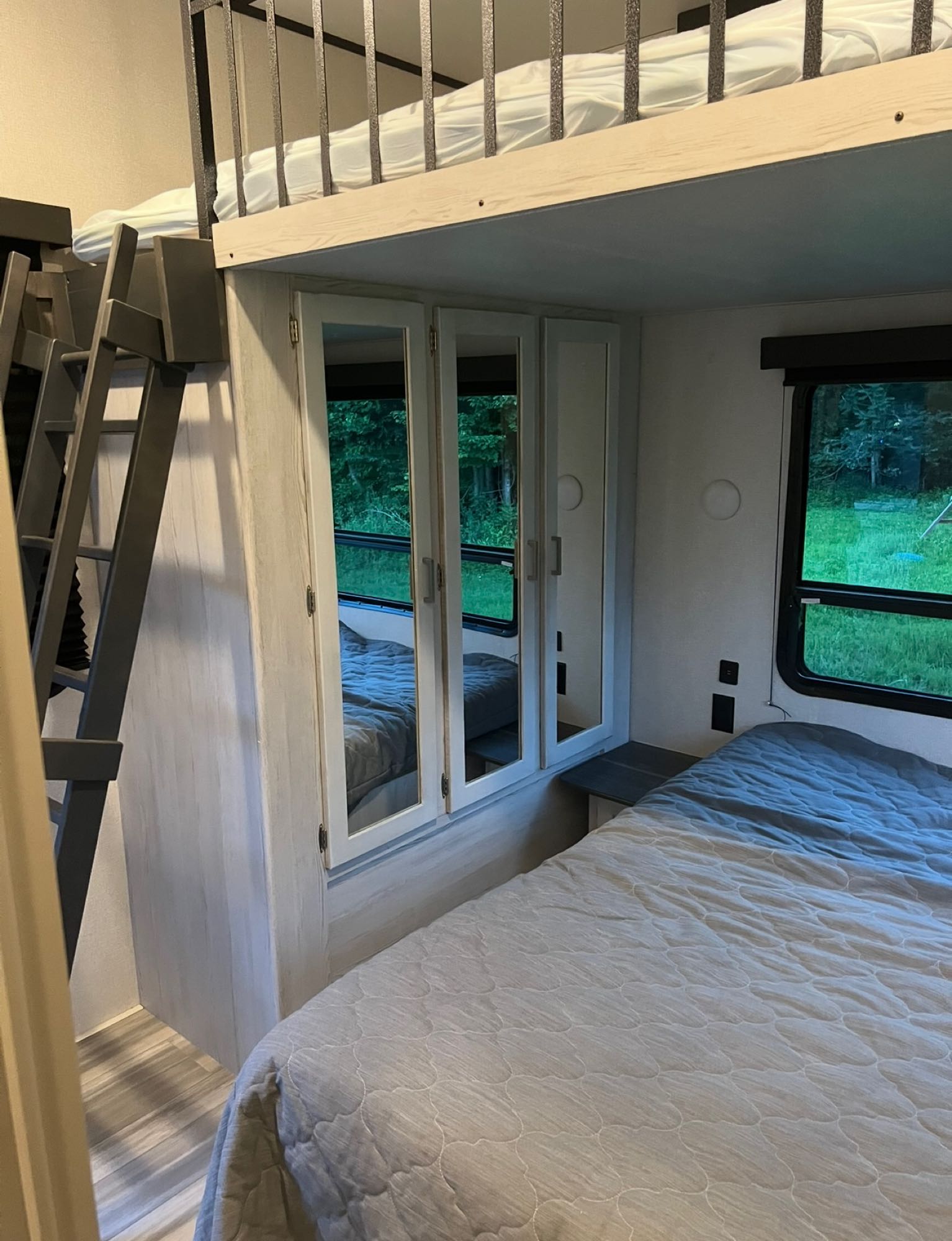 Modern RV rental bedroom with bunk beds, a ladder for access, and a main bed next to mirrored cabinets.. Keystone RV Sprinter Campfire Edition 2021