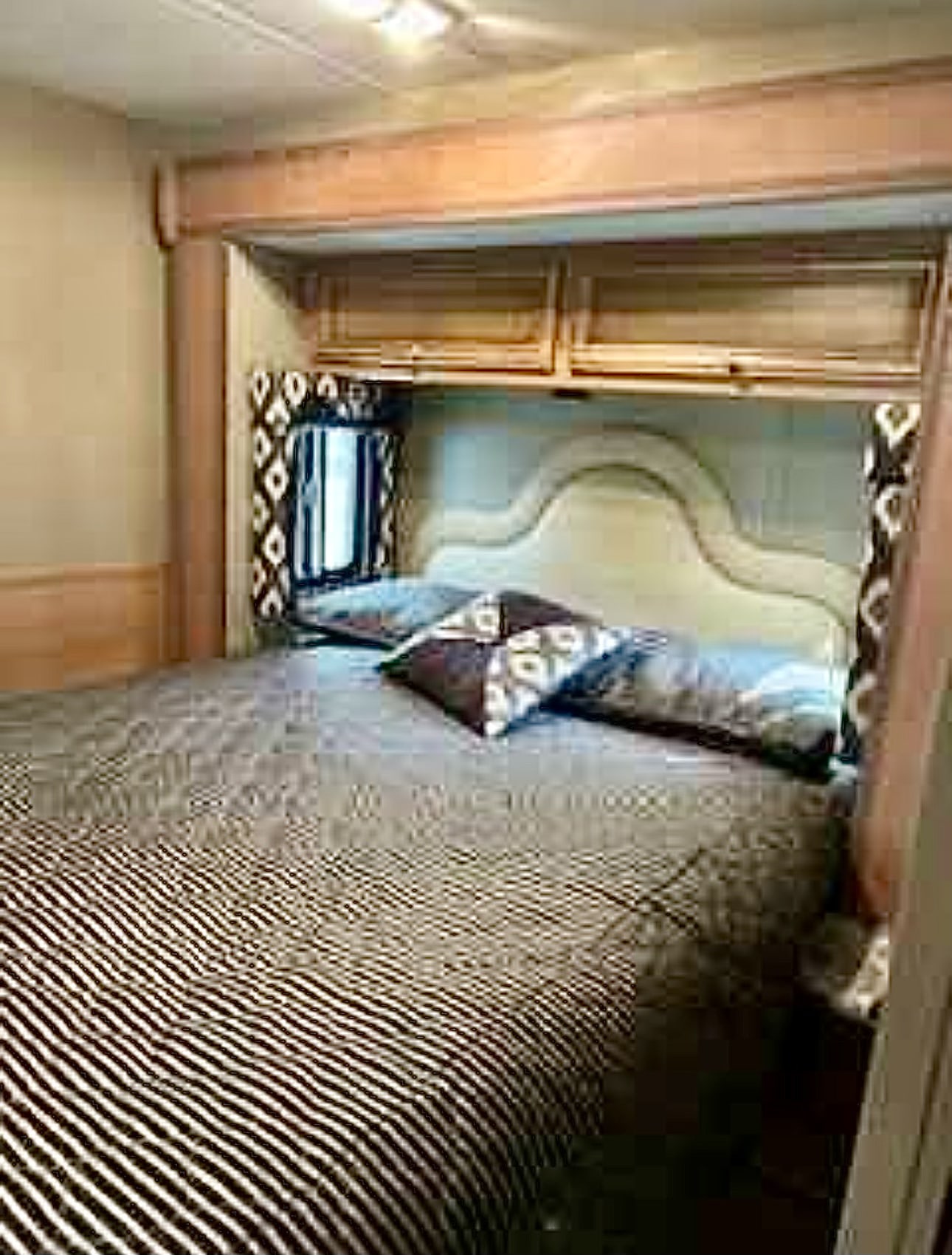 RV rental bedroom: Cozy bed with patterned comforter and pillows under wood cabinets.. Ford/Newmar Baystar Sport 2015