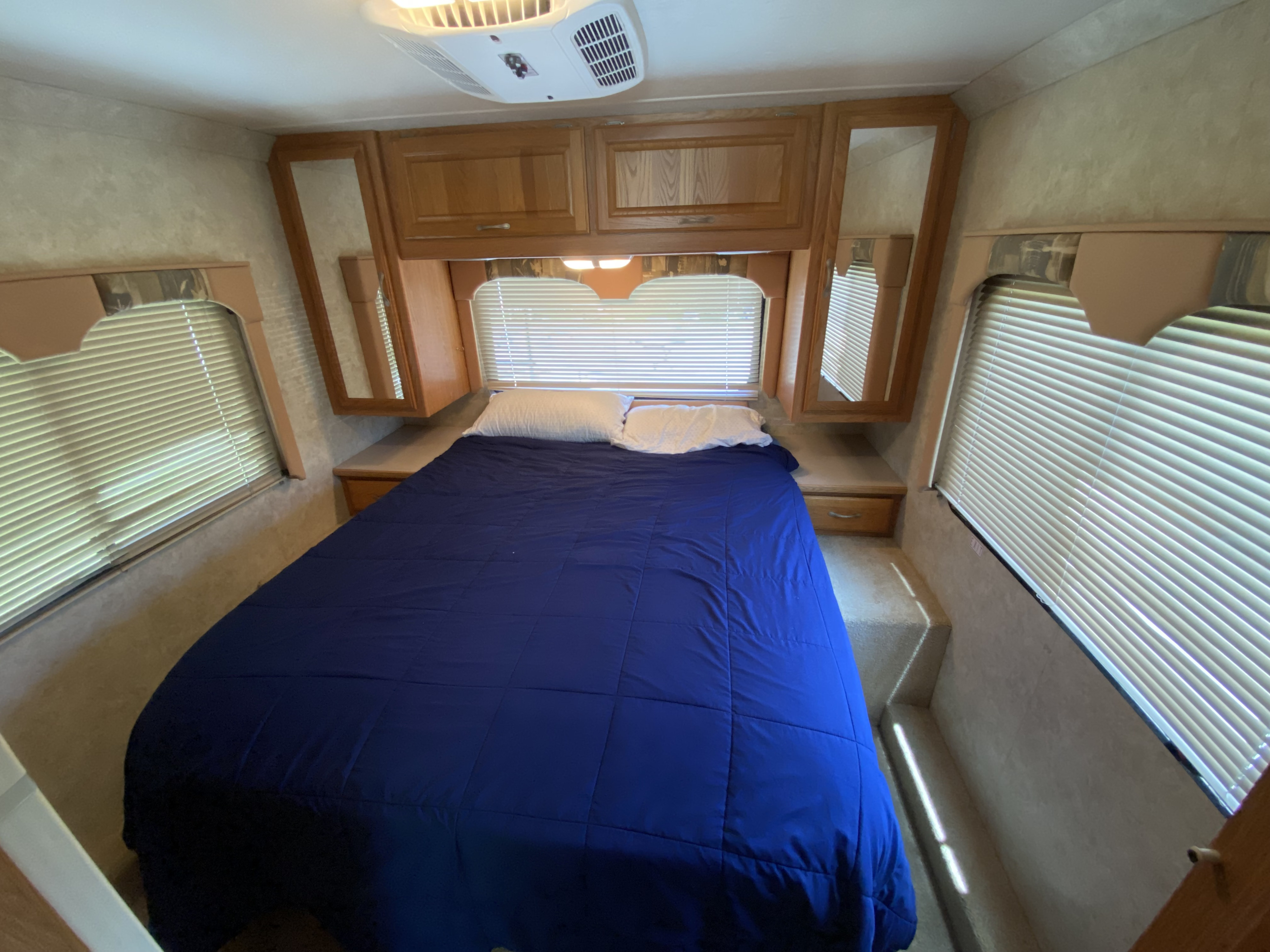 Step into comfort: this RV rental features a cozy bedroom with a blue bed, cabinets, AC, and window blinds.. Four Winds Hurricane 2005