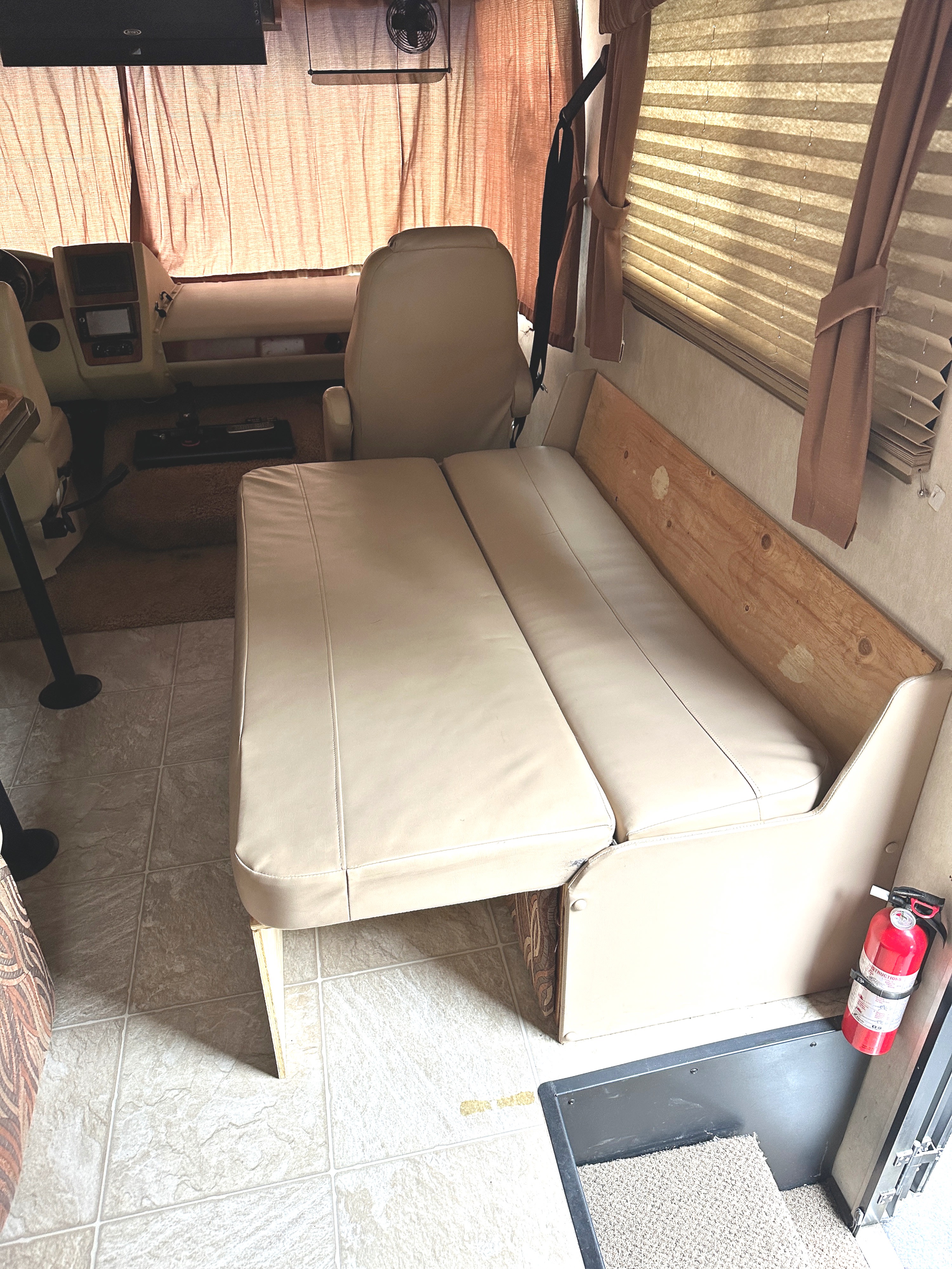 RV rental interior with beige convertible sofa, cockpit area, tiled floor, and red fire extinguisher.. Coachmen Mirada 2009