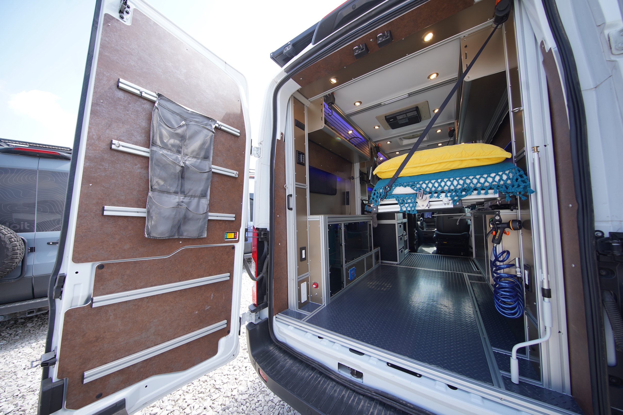 RV rental: detailed view of a camper van's organized rear cargo area, featuring modular storage, a raised bed, and utility hose.. Vandoit MOOV 2023