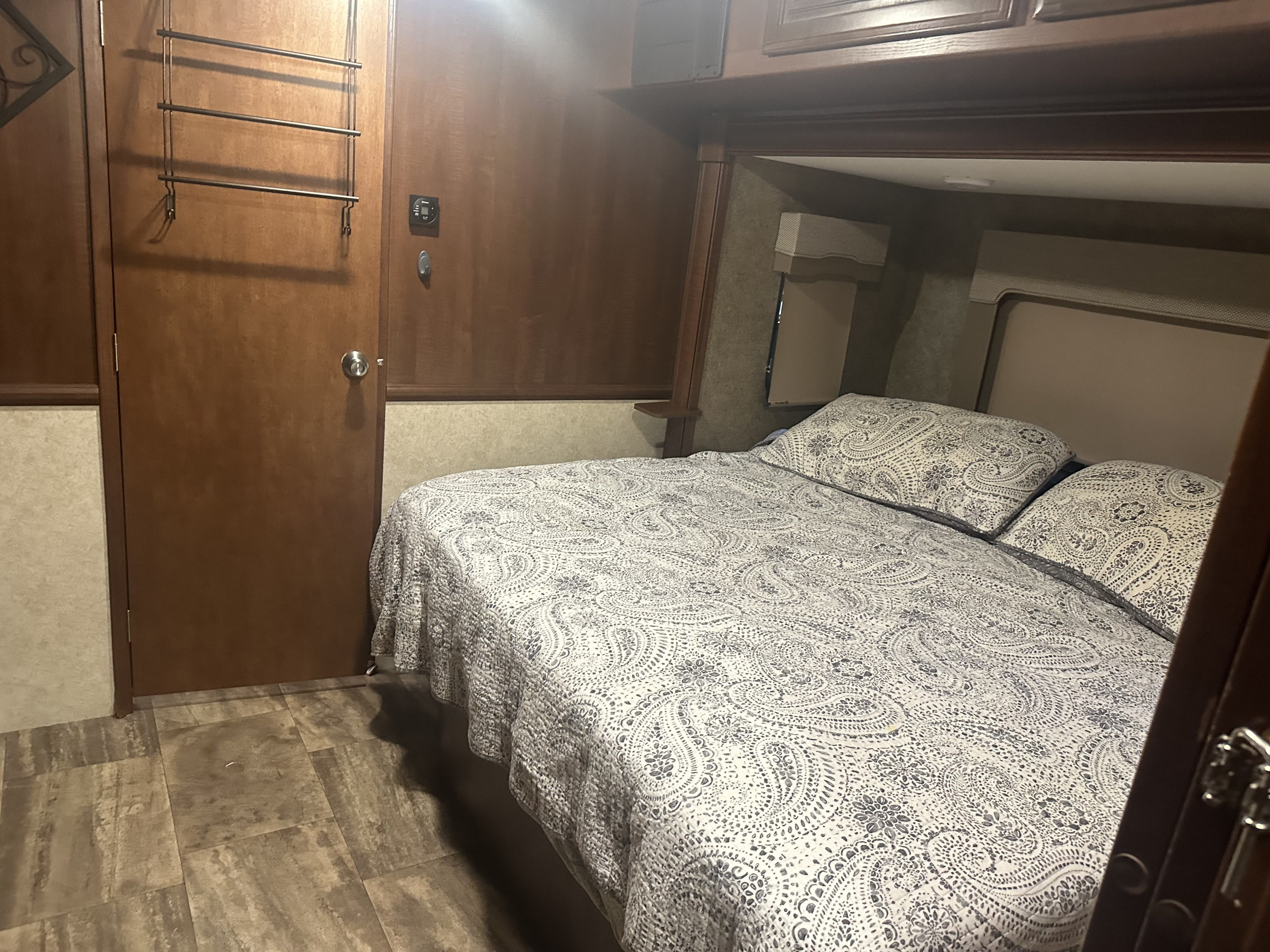 Cozy RV rental bedroom: patterned bed, wooden cabinetry, door rack, and visible thermostat.. Forest River Georgetown 2017