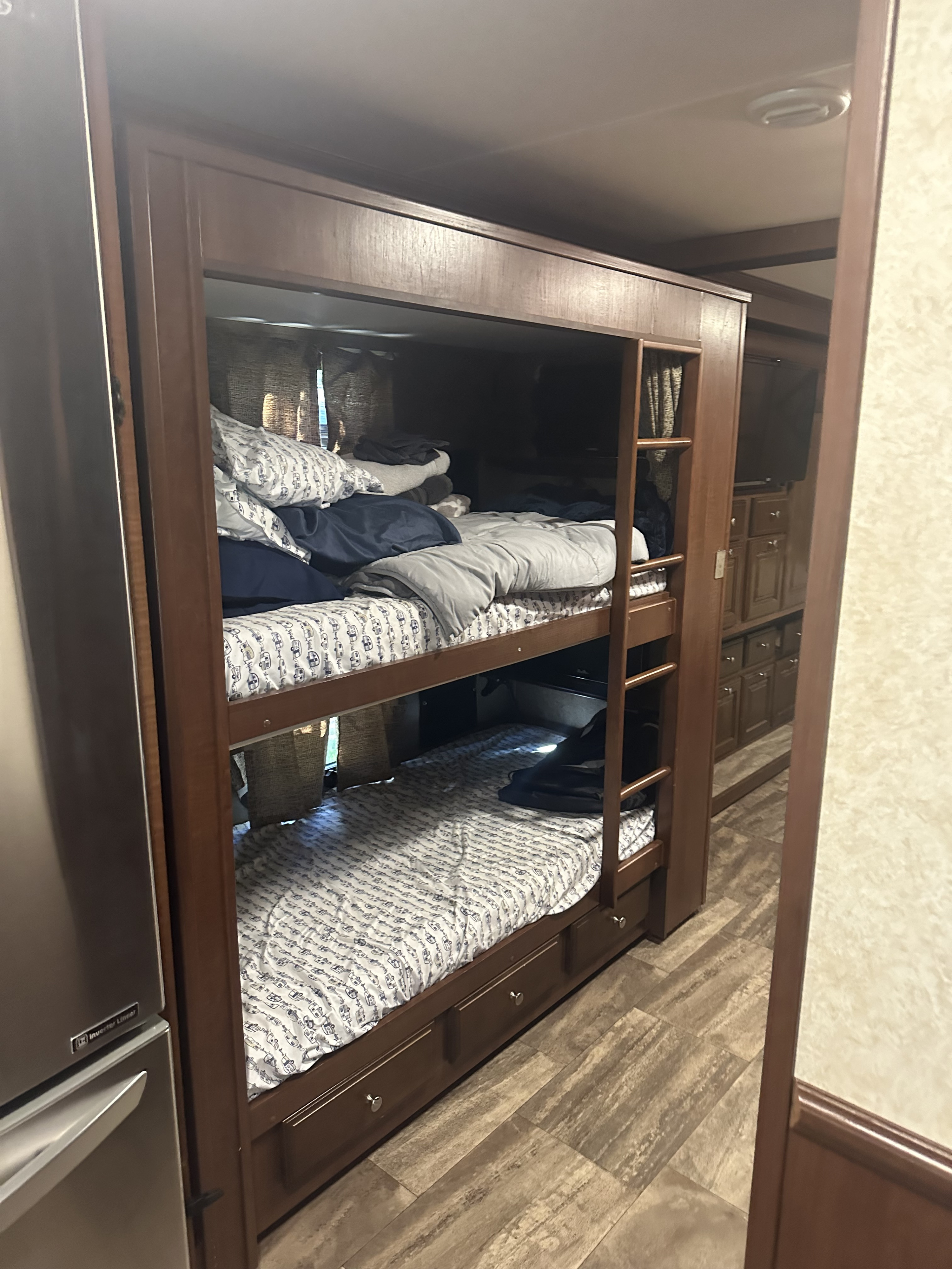 Cozy RV rental bunk bed area with patterned sheets, ladder, under-bed storage drawers, and a nearby refrigerator.. Forest River Georgetown 2017
