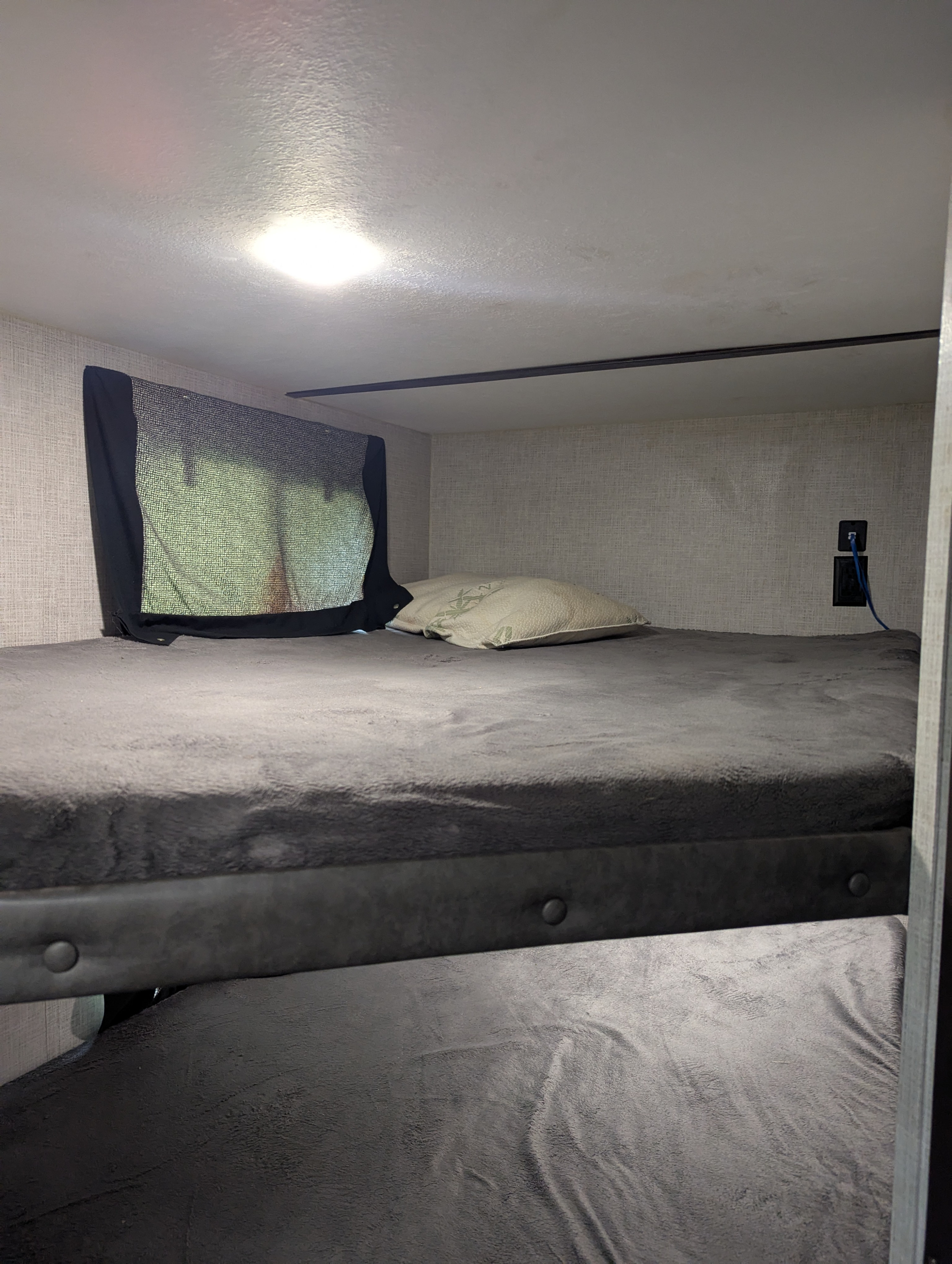 Cozy RV rental bunk beds with a window shade, pillow, and charging outlet. Provides comfortable sleeping space.. Keystone RV Bullet Crossfire 2020